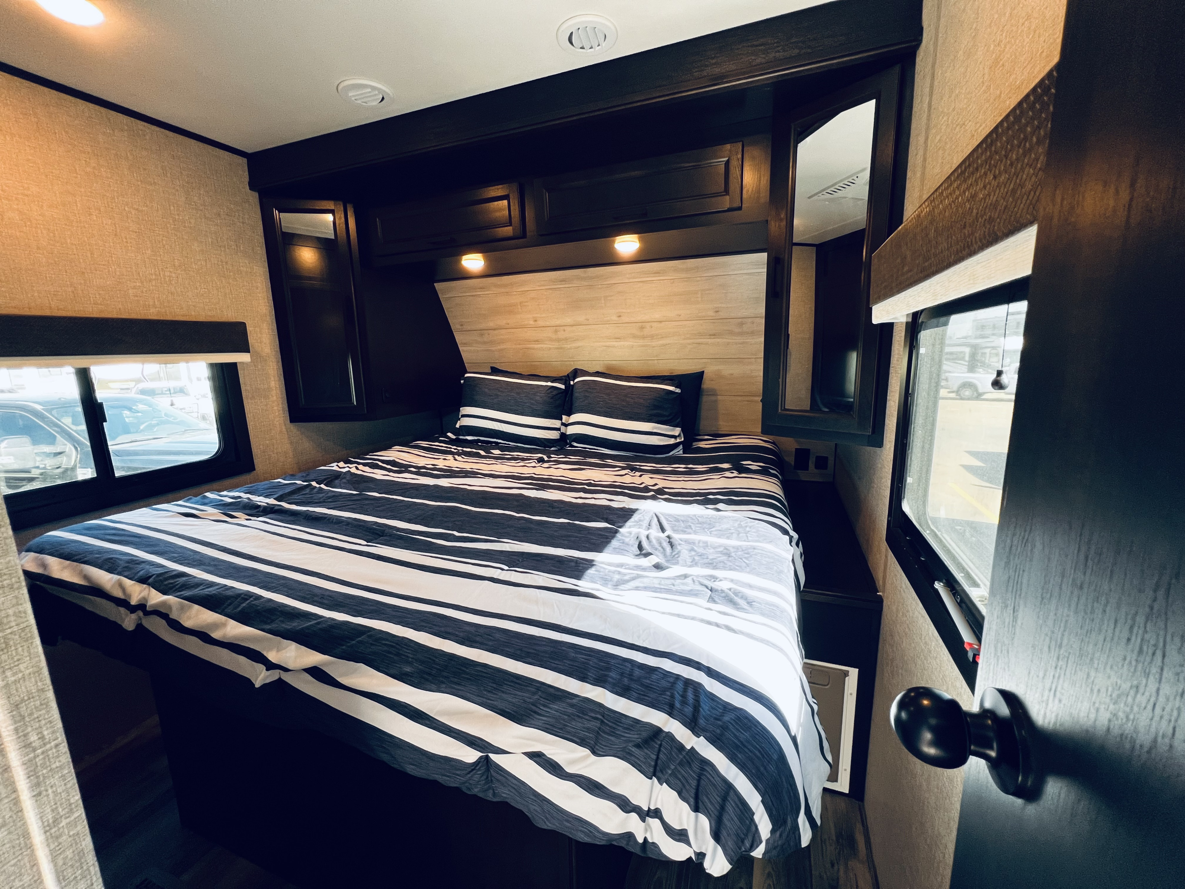 Cozy RV rental bedroom featuring a large bed with striped bedding, overhead storage, and windows for natural light.. Jayco Eagle 312 BHOK 2024