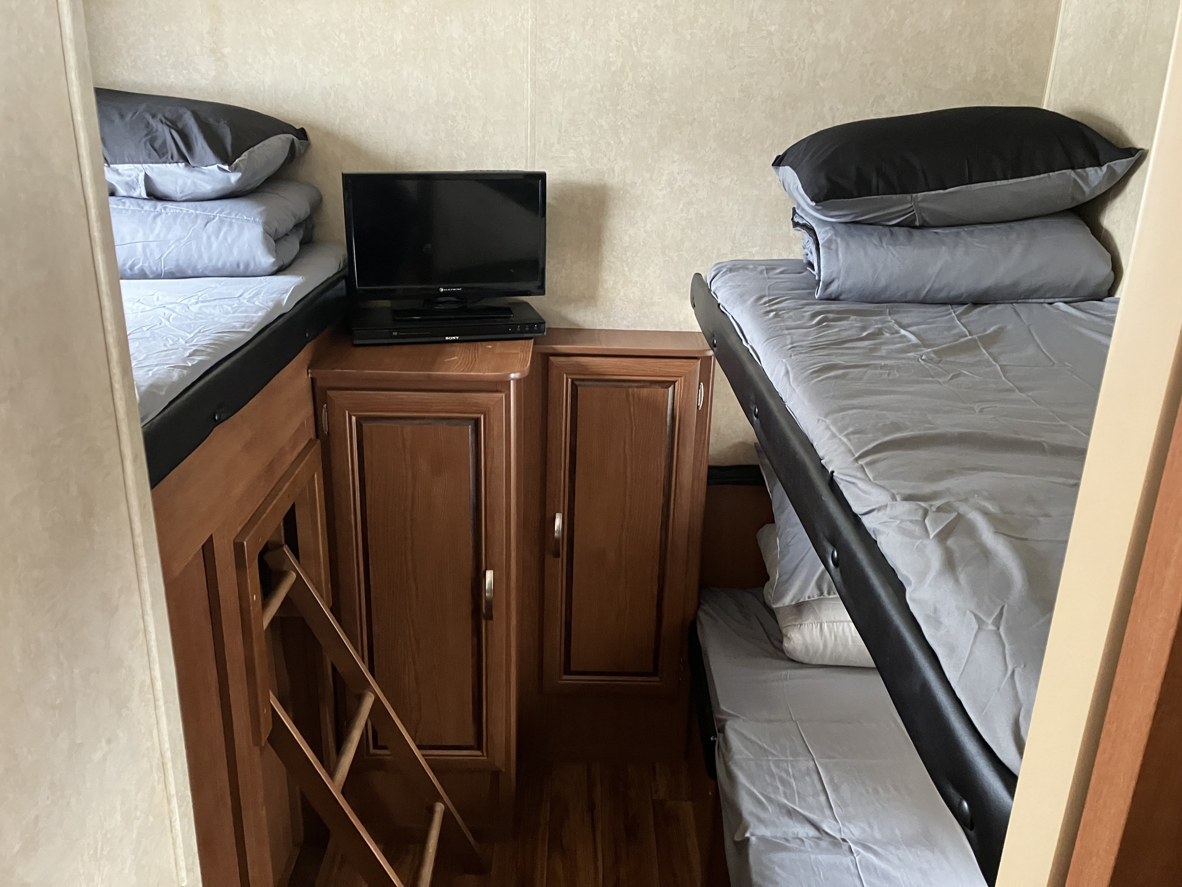 Cozy RV rental bunk room featuring stacked beds, a TV, DVD player, and wooden storage cabinets with a ladder.. Forest River Salem 2015