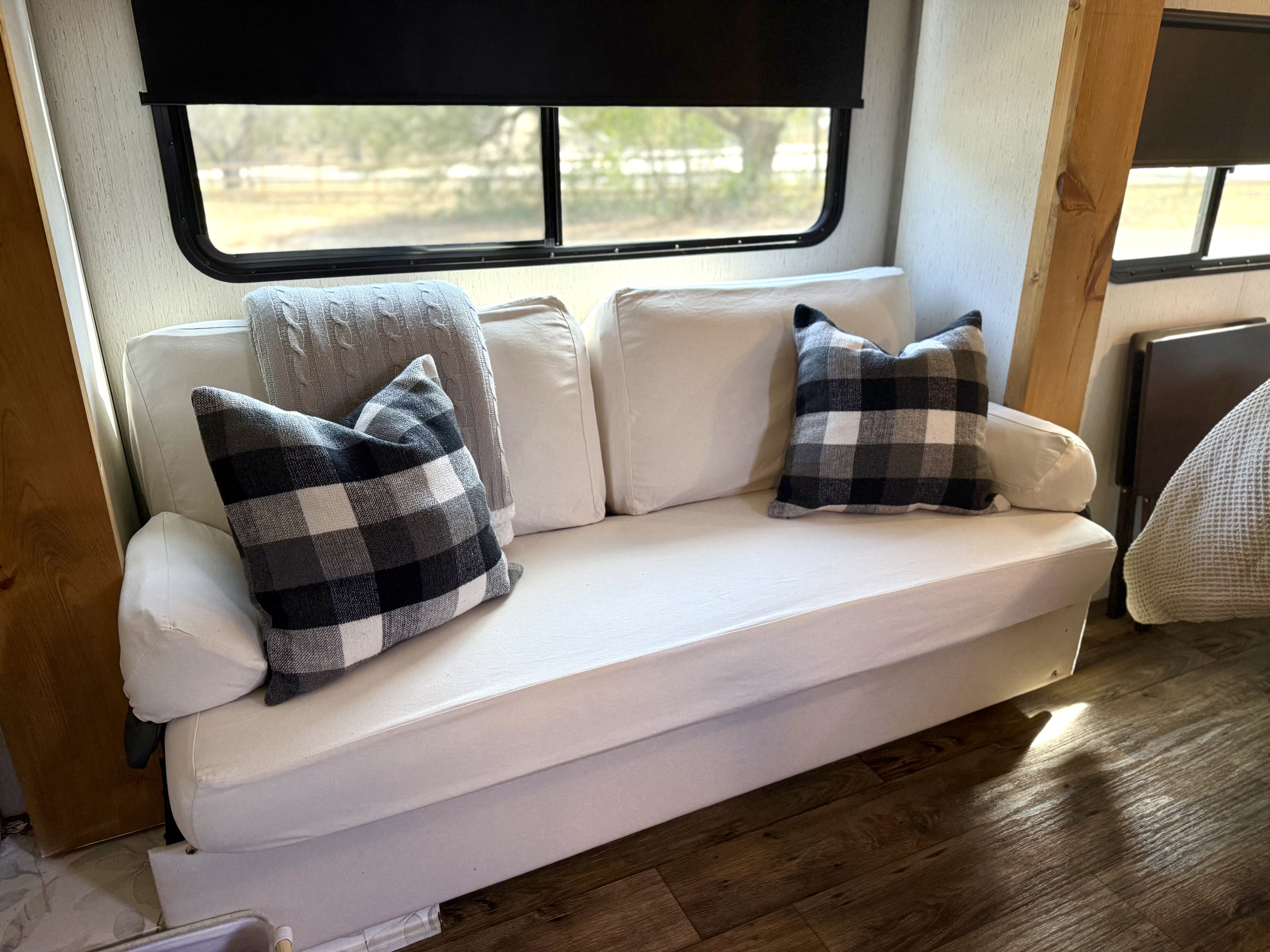 Comfortable white sofa with plaid pillows and a window view inside this cozy rv rental.. Dutchmen Kodiak Cub 2022