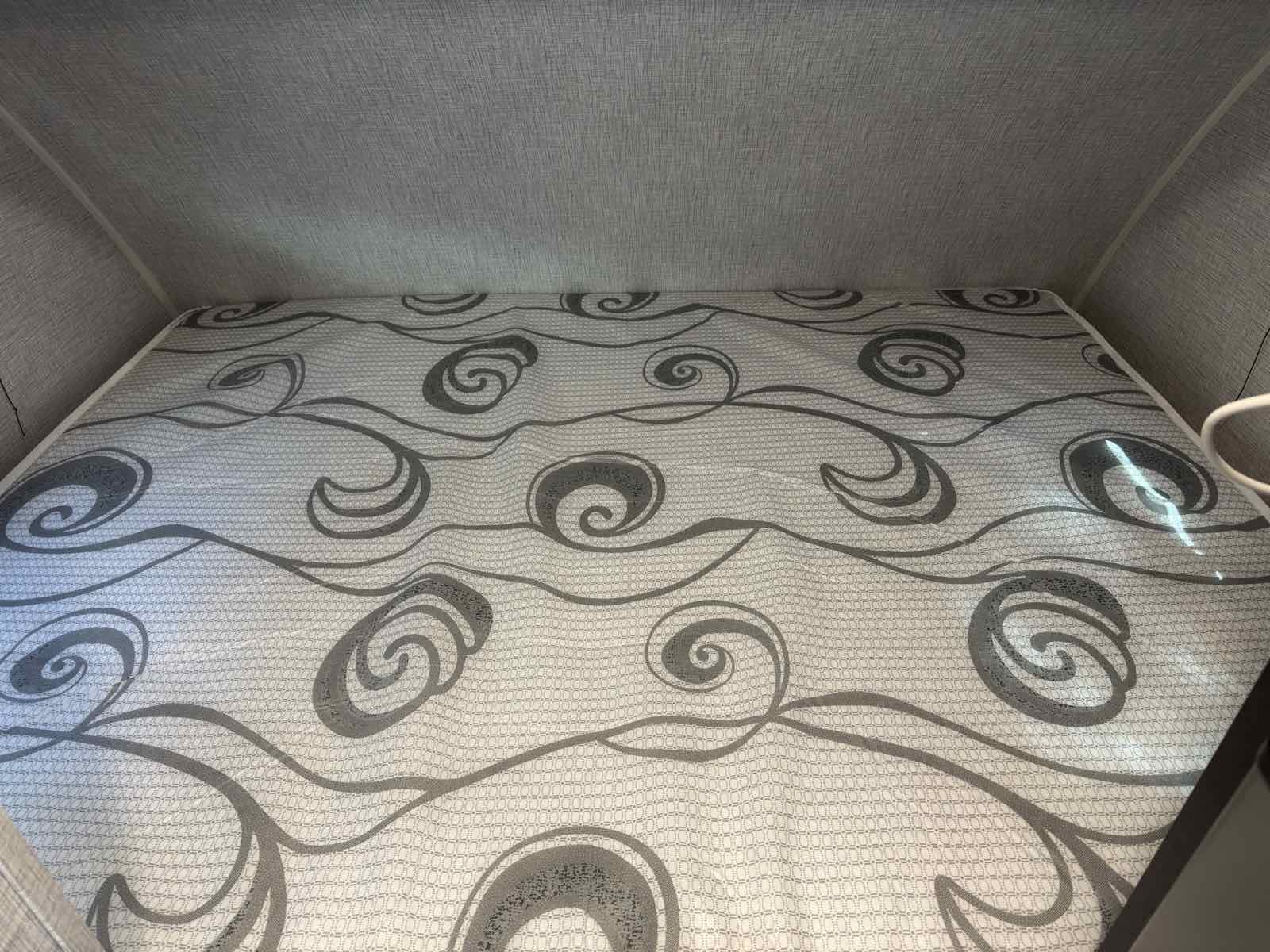 RV rental's cozy bed: A light mattress with an abstract grey swirling pattern, nestled in a compact sleeping area.. Braxton Creek Free Solo Plus 2022