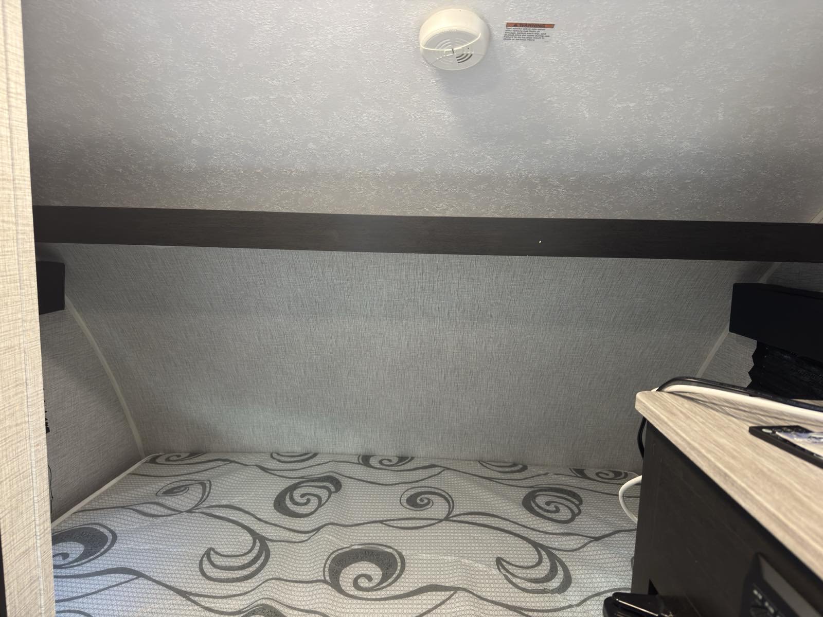Cozy RV rental sleeping area with a patterned mattress, light textured walls, and a ceiling-mounted smoke detector.. Braxton Creek Free Solo Plus 2022