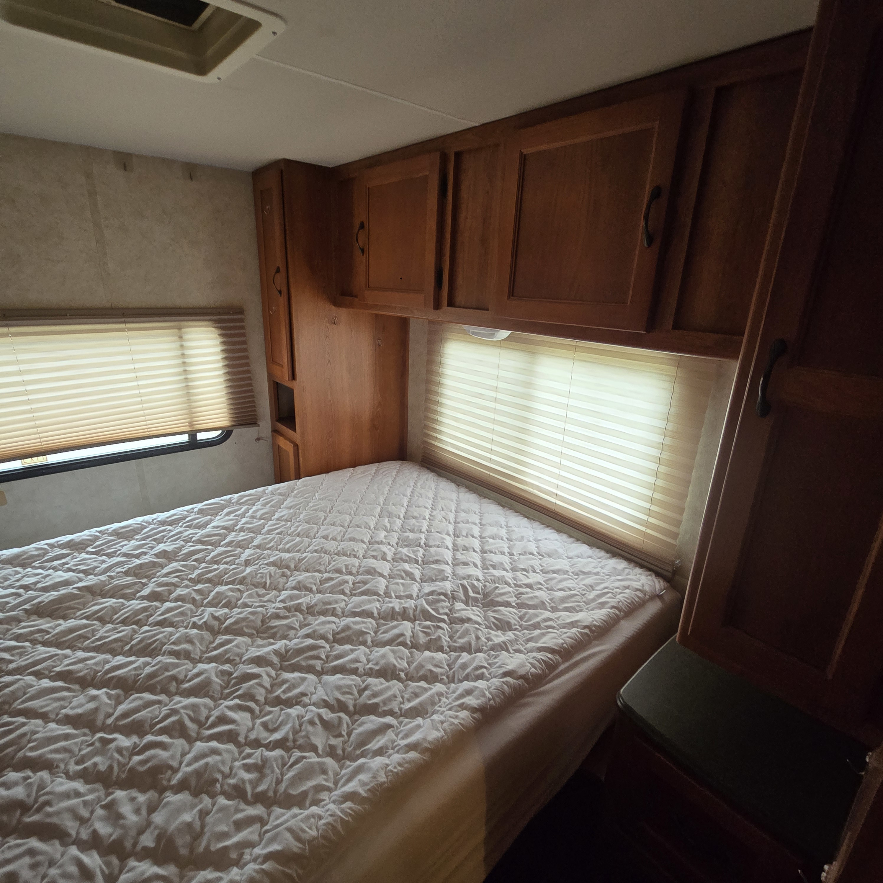 This RV rental bedroom features a comfy bed with quilted mattress, wooden cabinets, and windows with blinds, ideal for your next trip.. Coachmen Freelander 2011