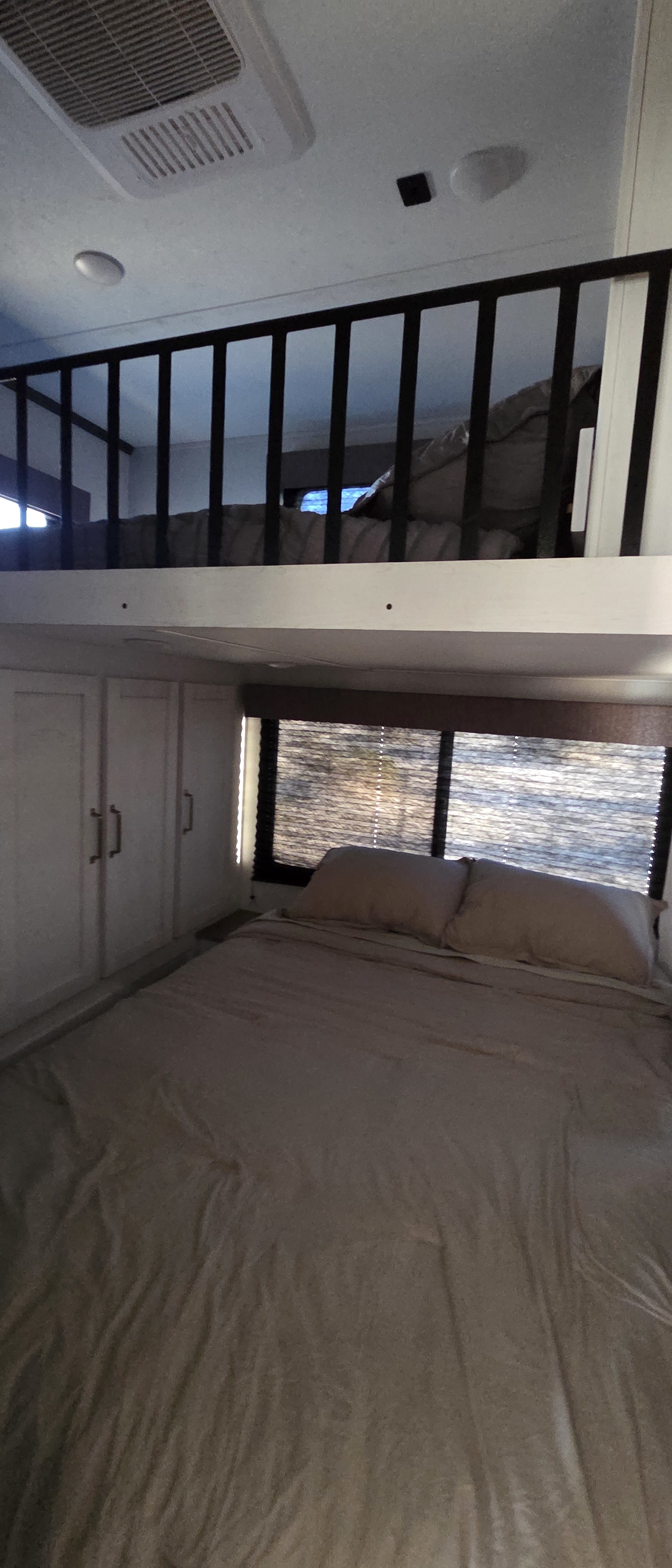 RV rental interior: A cozy lower bedroom with a large bed, cabinets, and a scenic window below a charming loft sleeping area.. Astoria Astoria Fifth Wheel 2023