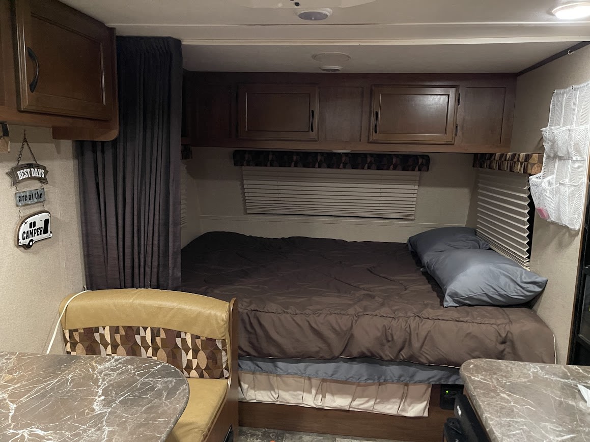 Cozy RV rental bedroom with brown bedding, overhead storage, and a small dining area on the left.. Jayco Jay Flight Swift SLX 2014