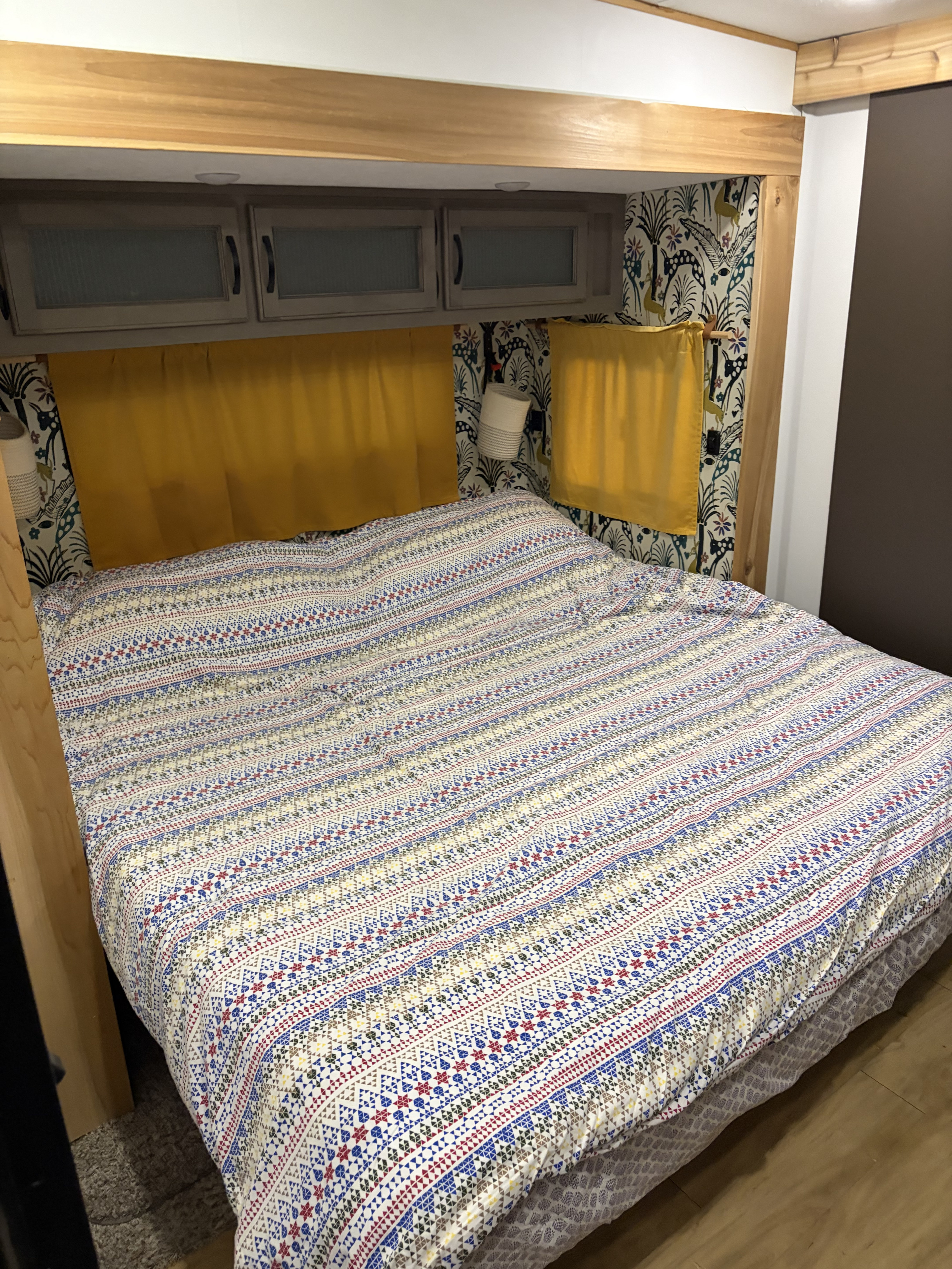 Cozy RV rental bedroom features a vibrant patterned bed, overhead cabinets, and playful wallpaper, providing comfort for travelers.. Forest River Coachmen Chaparral Lite 2022