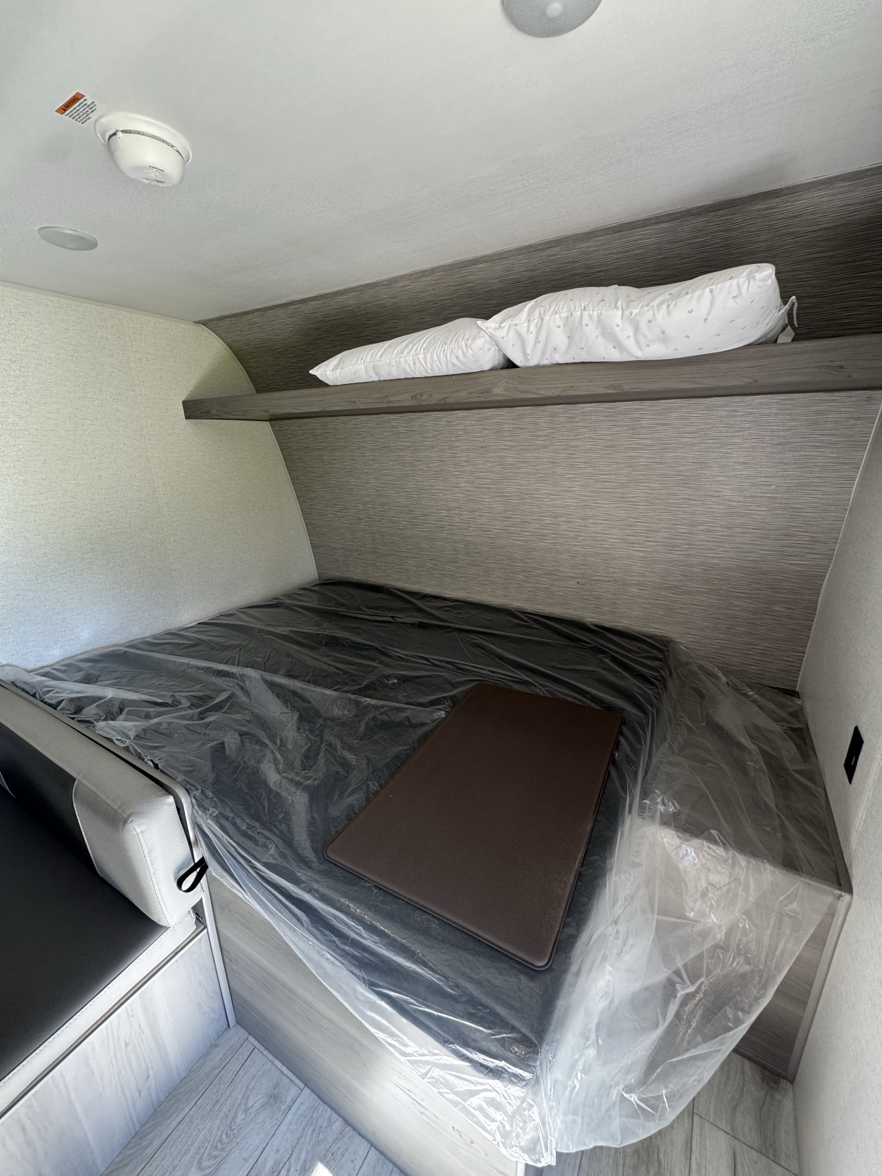 This RV rental features a bunk/dinette bed with a new, plastic-covered mattress, pillows on a shelf, and a smoke detector on the ceiling.. Keystone RV Hideout Sport 2025