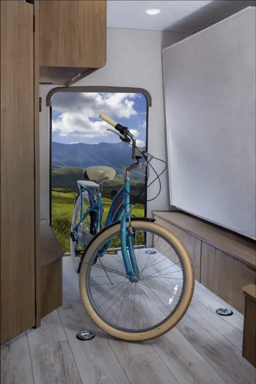 This RV rental's cargo area showcases a blue bicycle against a mountain view. Perfect for adventure and gear transport.. Forest River Coachmen Leprechaun 2024