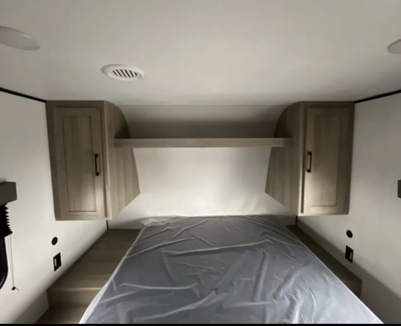 RV rental bedroom interior: Bed with protective cover, modern overhead cabinets, and a shelf, featuring ceiling lights and vents.. Keystone Coleman 2025