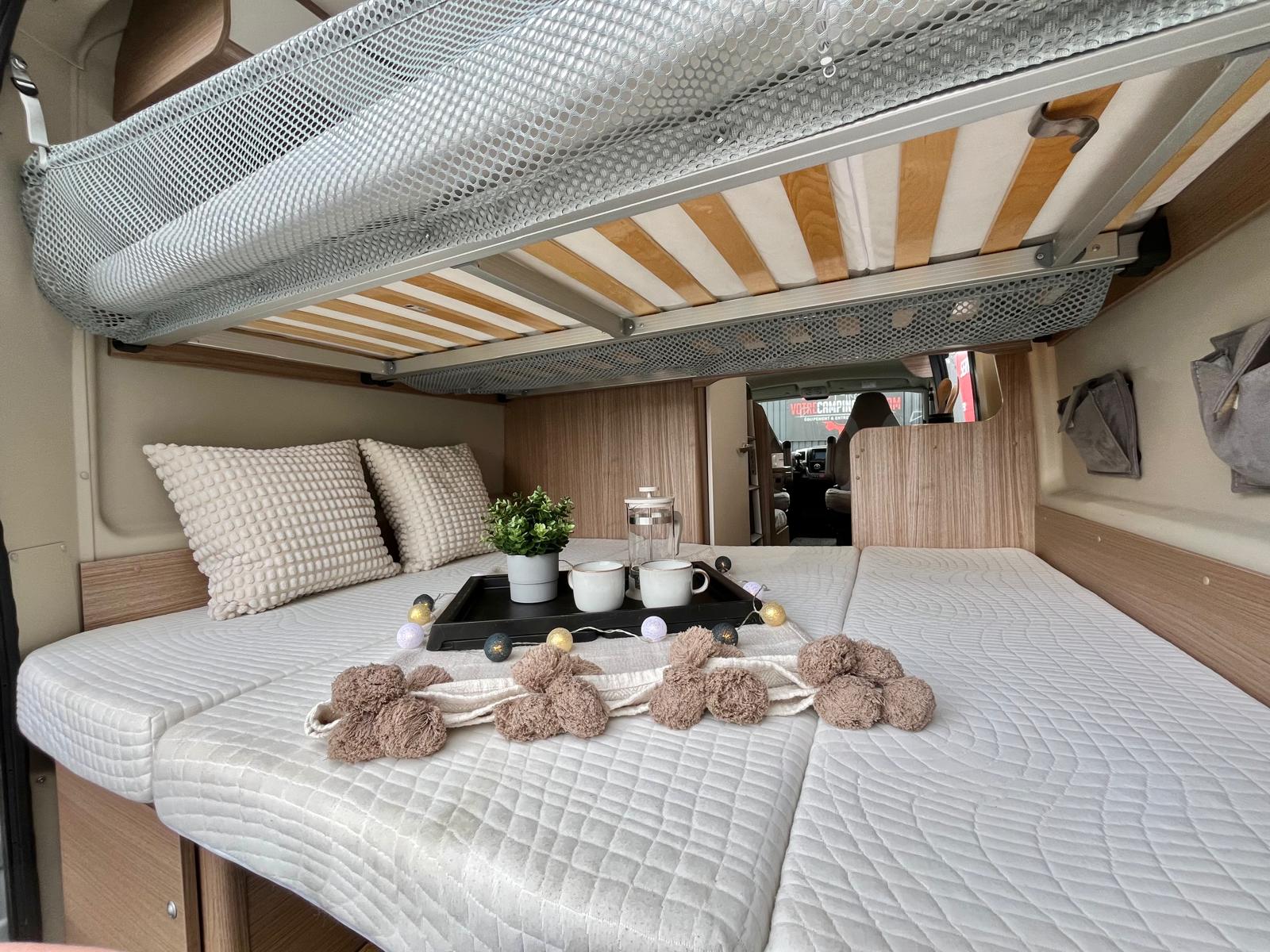Cozy rv rental interior: comfortable bed with pillows, decor, and an upper bunk, ready for your next adventure.. CARADO CV 601 2021