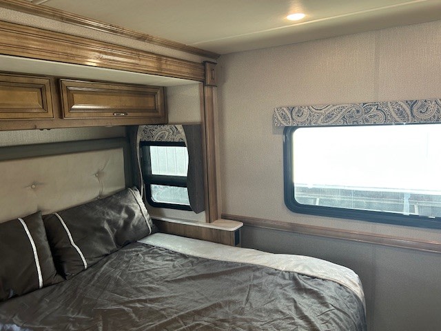 Cozy RV rental bedroom interior featuring a comfy bed, padded headboard, wooden cabinets, and windows, ideal for travel comfort.. Bounder Bounder Motorhome 2019