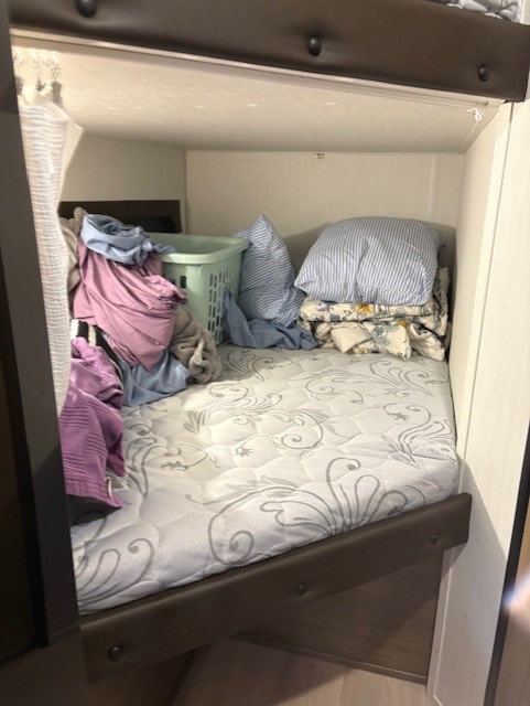 Inside an RV rental, a bunk bed is piled with laundry, a green basket, pillows, and blankets, needing a tidy.. Forest River Cherokee Wolf Pup Black Label 2025