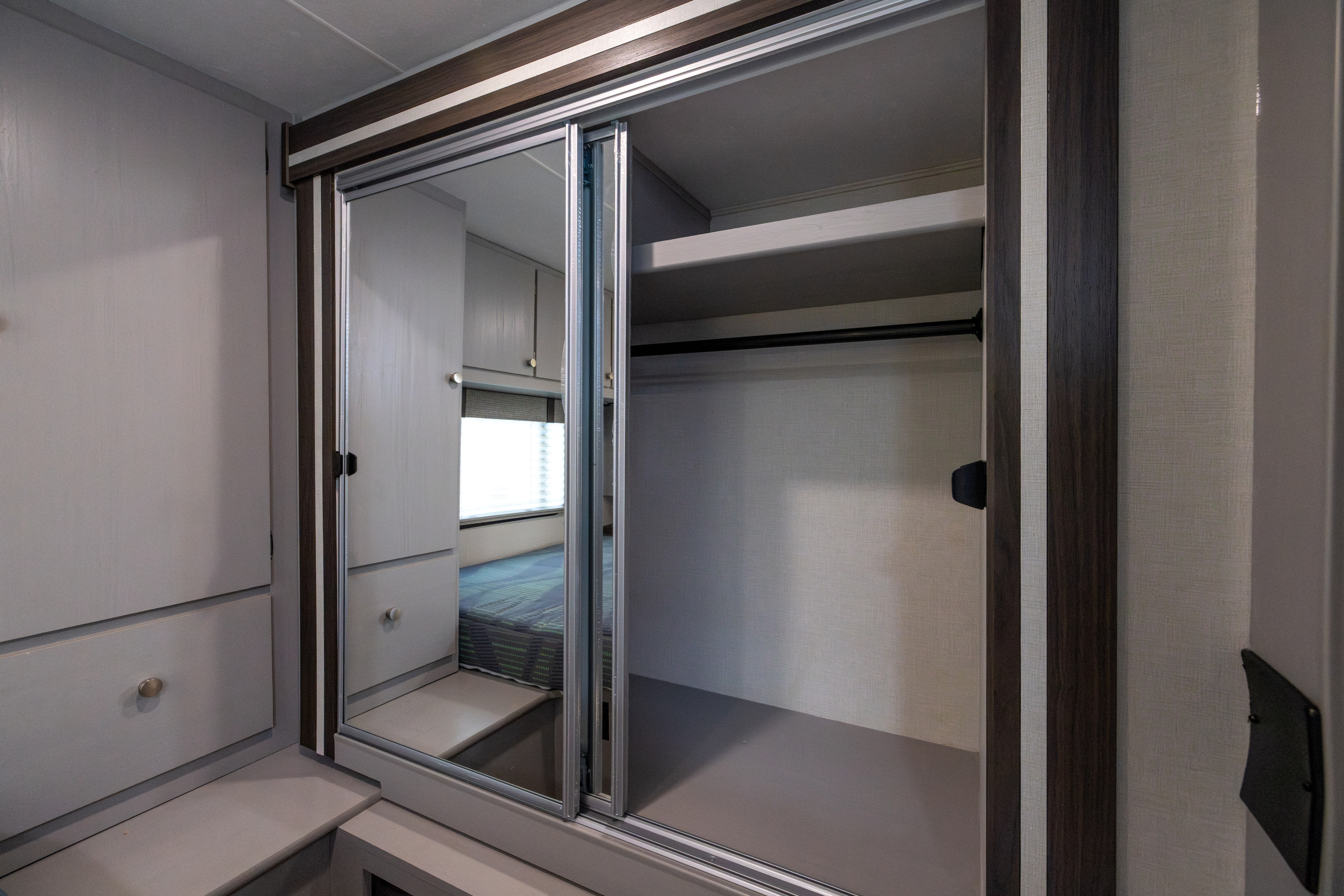RV rental wardrobe with mirrored sliding doors, shelf, and hanging rod, offering efficient storage in a compact bedroom space.. Coachmen Freelander 2027
