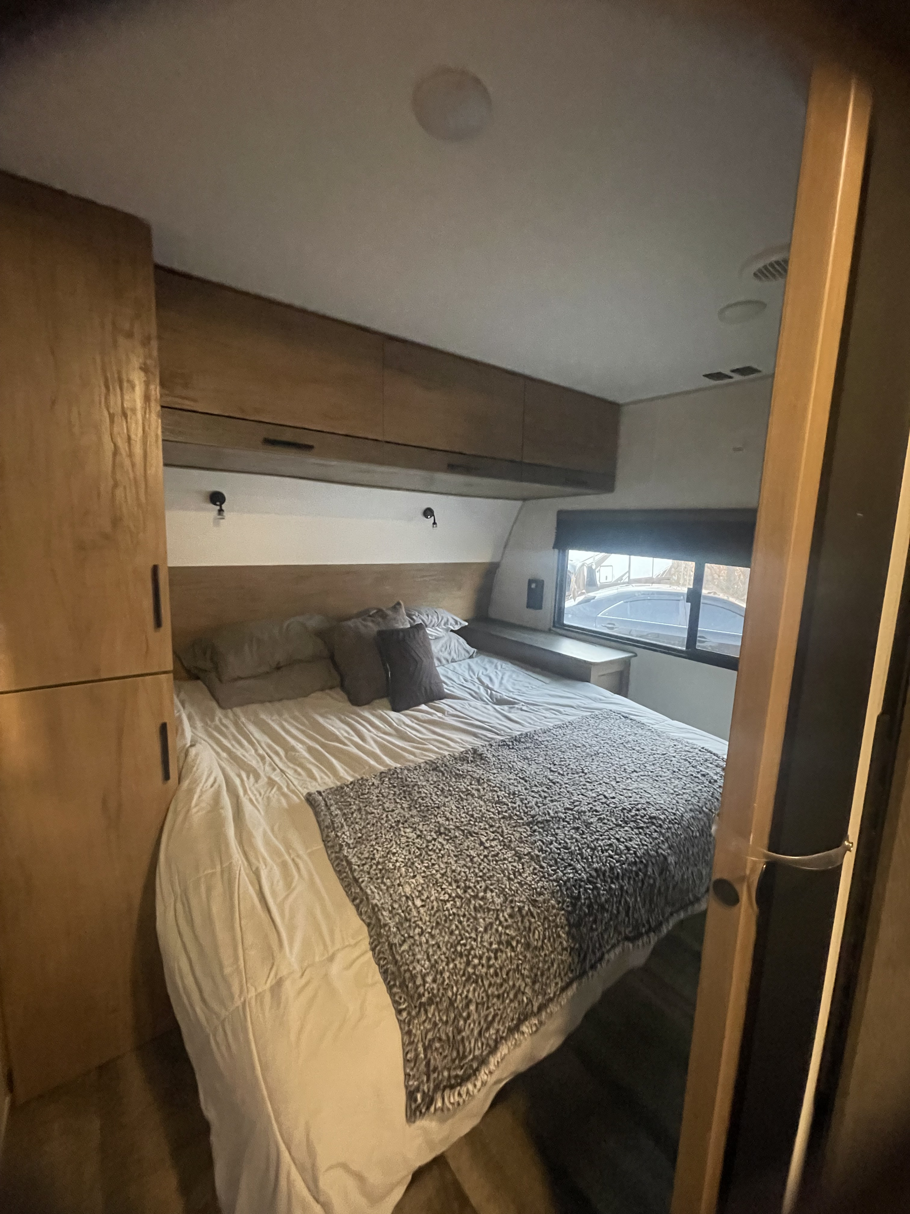 Cozy rv rental bedroom with a comfortable bed, overhead cabinets, reading lights, and a window view.. Forest River Campsite Reserve 2025