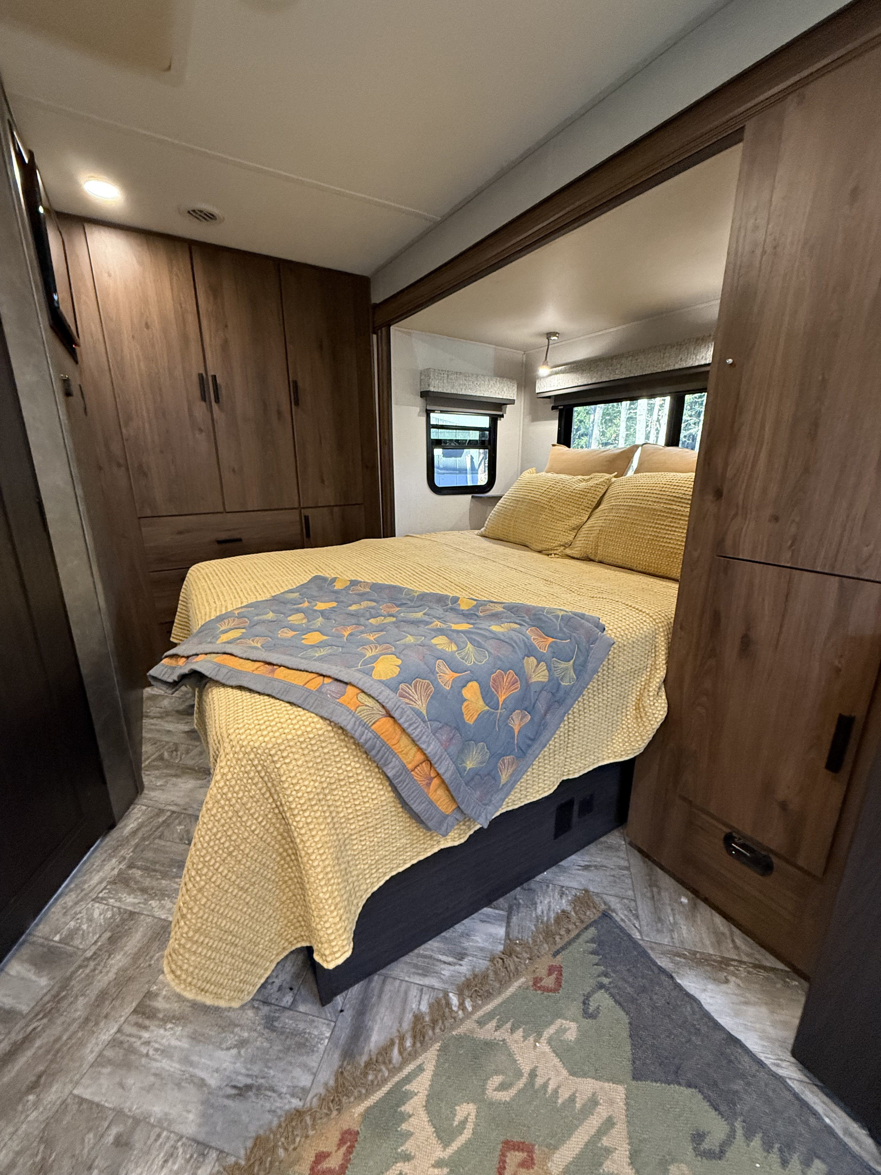 Cozy RV rental bedroom with warm yellow bedding, wooden cabinets, and windows showing trees.. Forest River Sunseeker MBS 2022