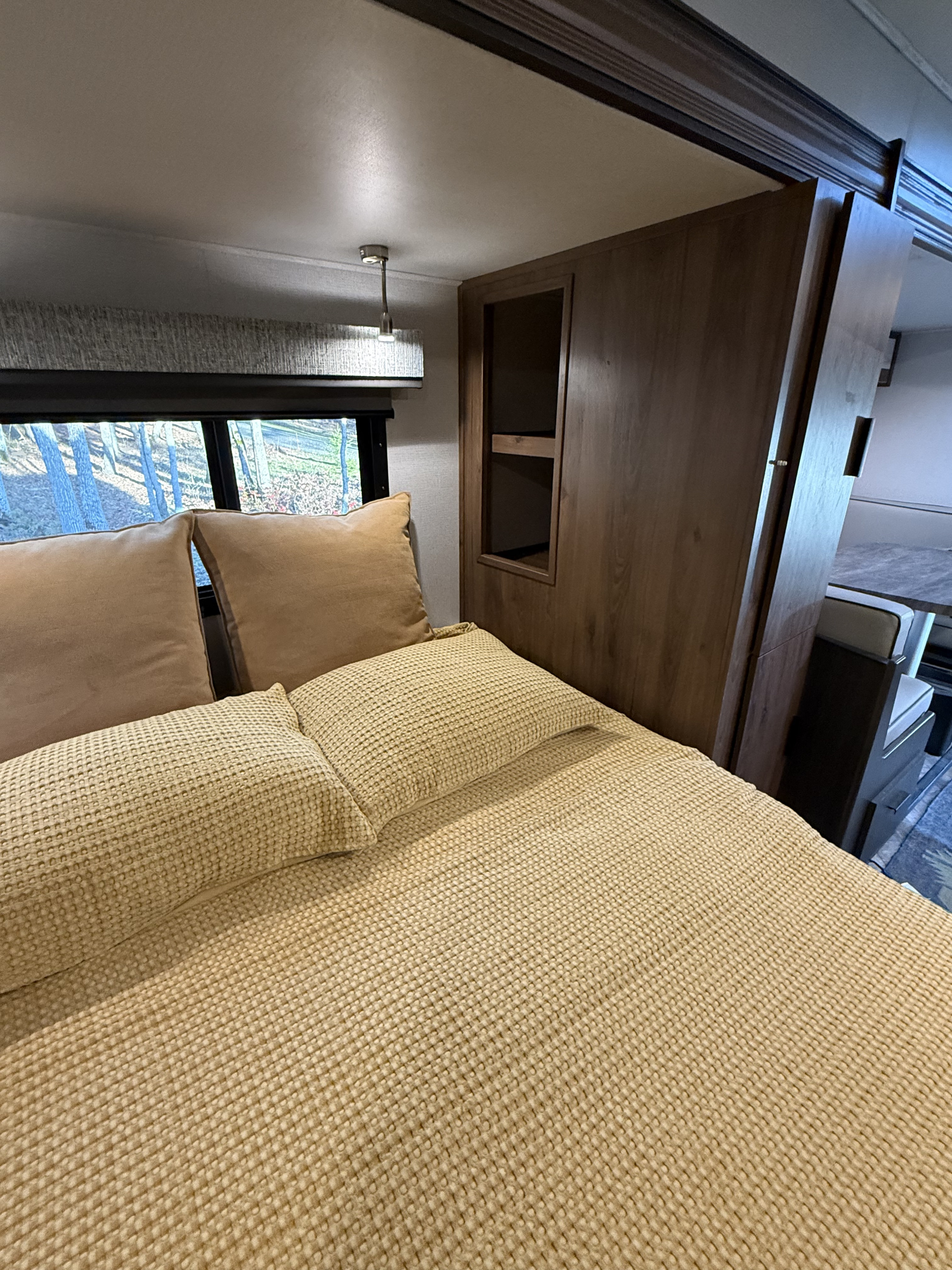 Inside an **rv rental**: a cozy bedroom with a textured bed, window showing trees, and wood finishes.. Forest River Sunseeker MBS 2022