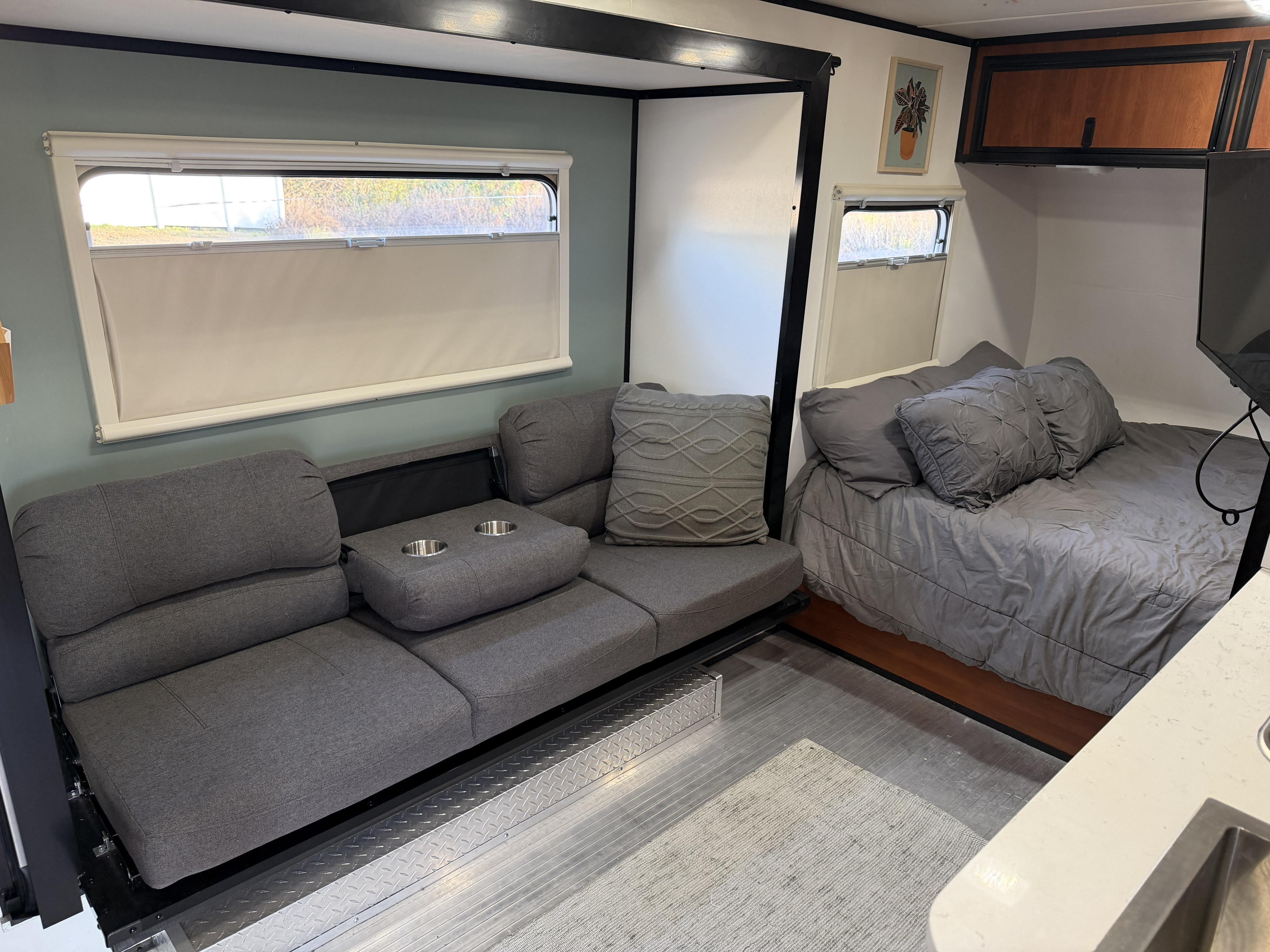 Inside a modern rv rental, featuring a gray sofa with cup holders, a cozy bed, and practical storage solutions.. Camp Lite Camp Lite Trailer 2014