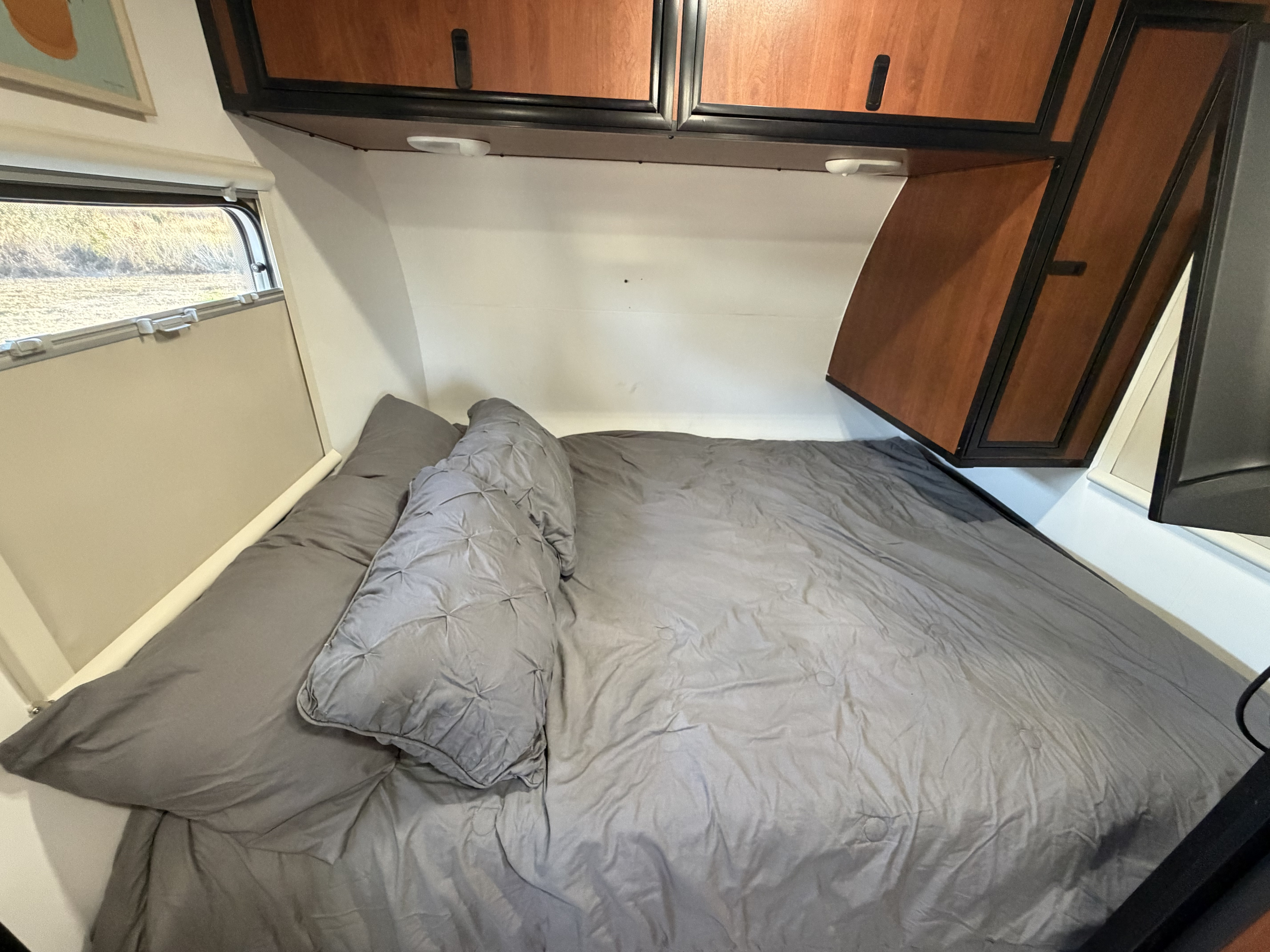 Cozy sleeping area inside an RV rental, featuring a comfortable gray bed, cabinets, and a window for natural light.. Camp Lite Camp Lite Trailer 2014