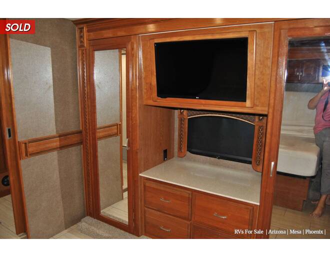 Spacious RV rental bedroom featuring a TV, wood cabinets, mirrored wardrobe, and dresser. Ideal for comfortable travel.. Holiday Rambler Endeavor 2018