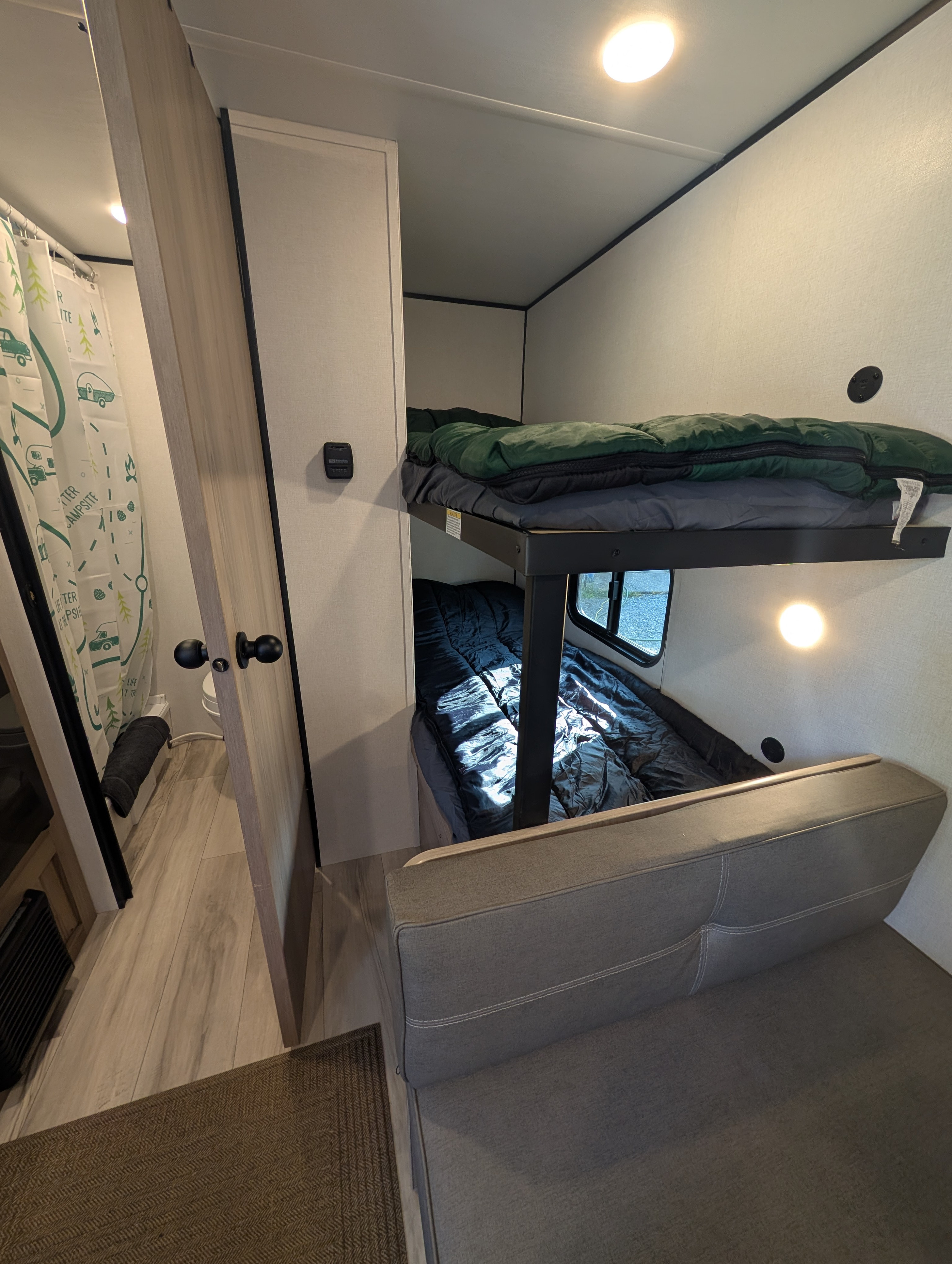 Compact RV rental interior featuring bunk beds with sleeping bags, a cozy couch, and a peek into the bathroom area.. Keystone RV Coleman 2026