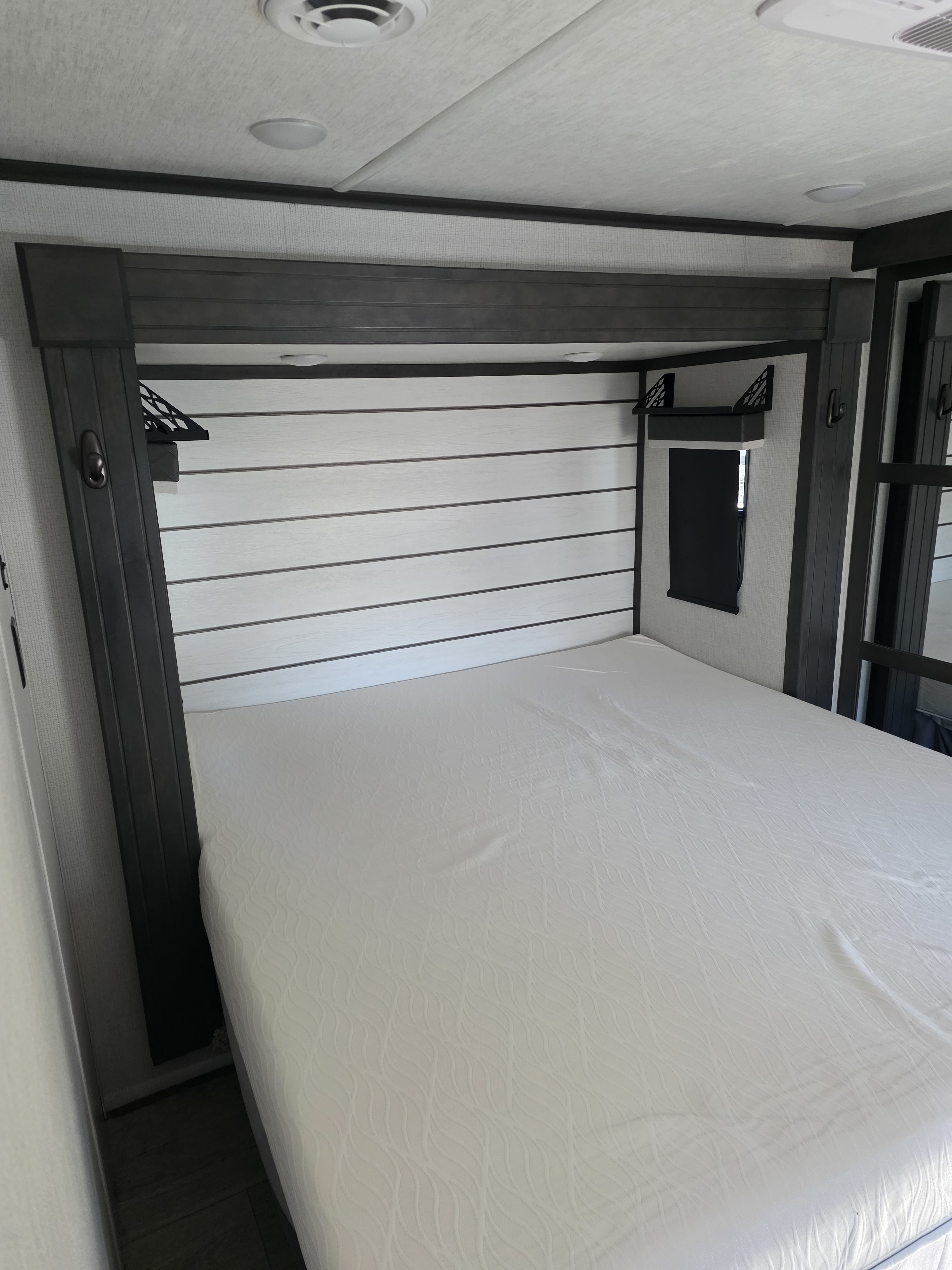 **RV rental bedroom:** A clean, modern RV sleeping area features a white bed, wood slat headboard, and overhead lighting.. Keystone RV Cougar 2024