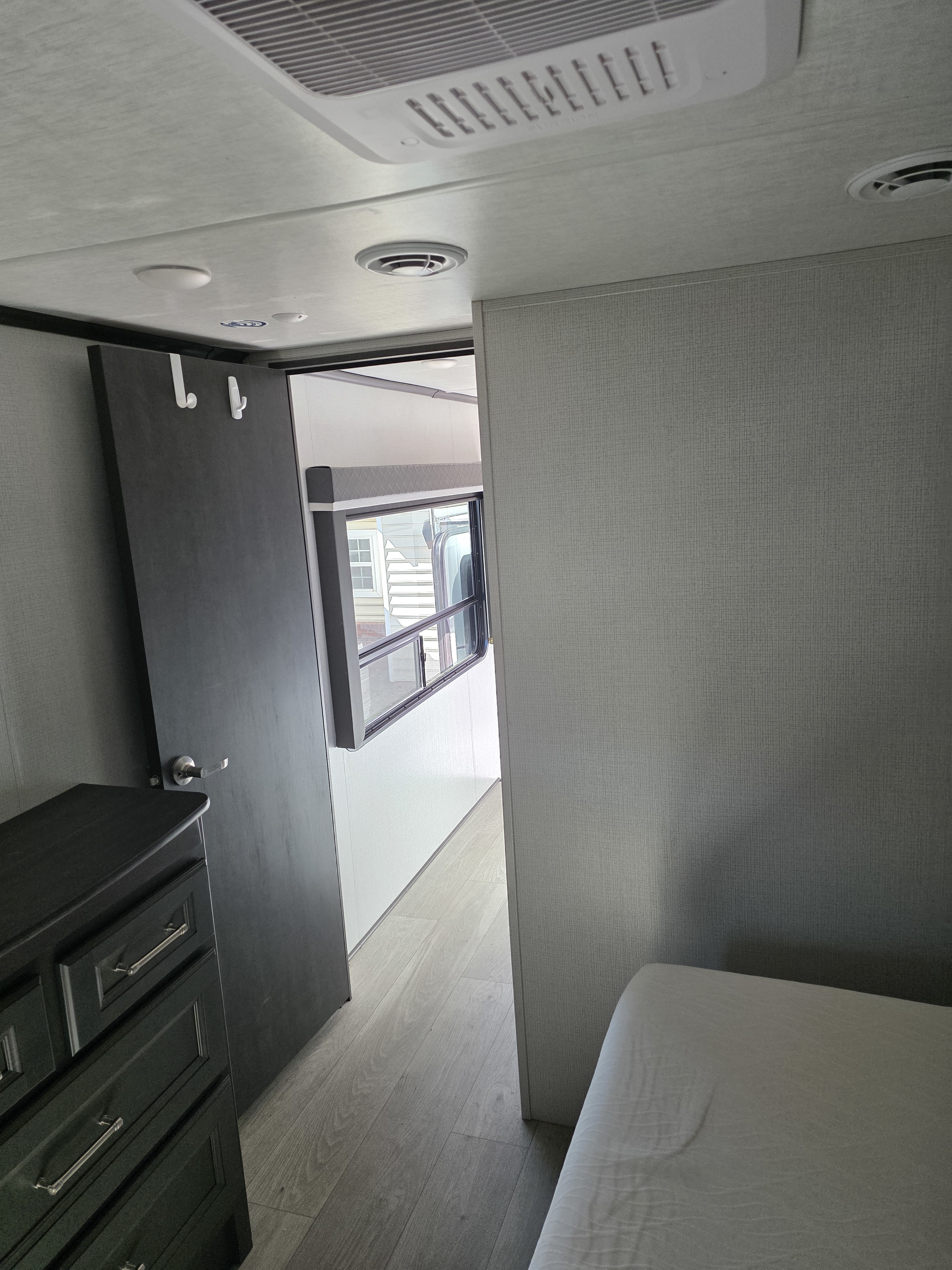 Inside an RV rental, showing a bedroom or living area with a dresser, sliding door, window, and ceiling vents.. Keystone RV Cougar 2024