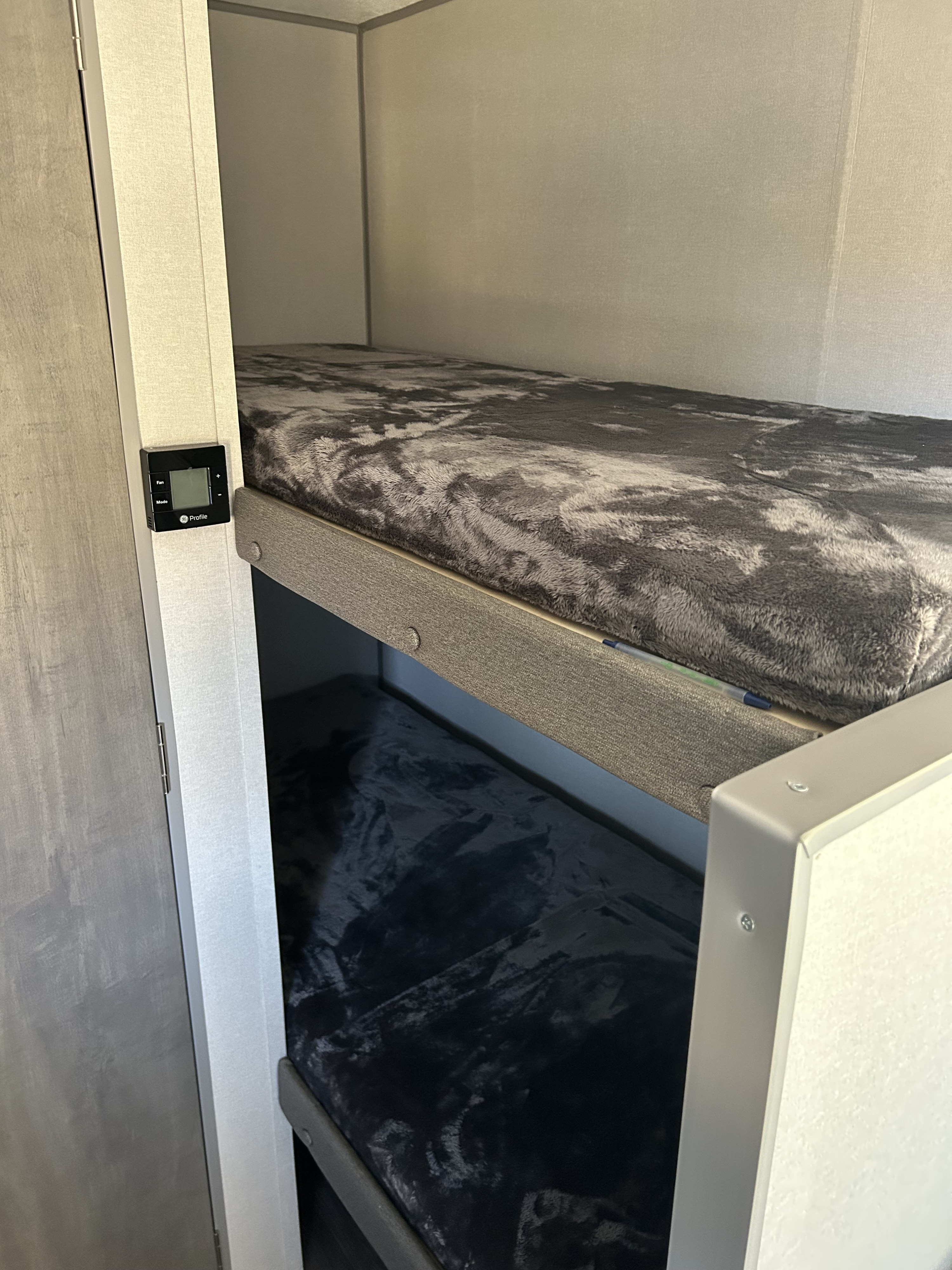 Interior of an **rv rental** showing stacked bunk beds with soft gray blankets, beside a GE Profile climate control panel.. Forest River Aurora Aurora 2026