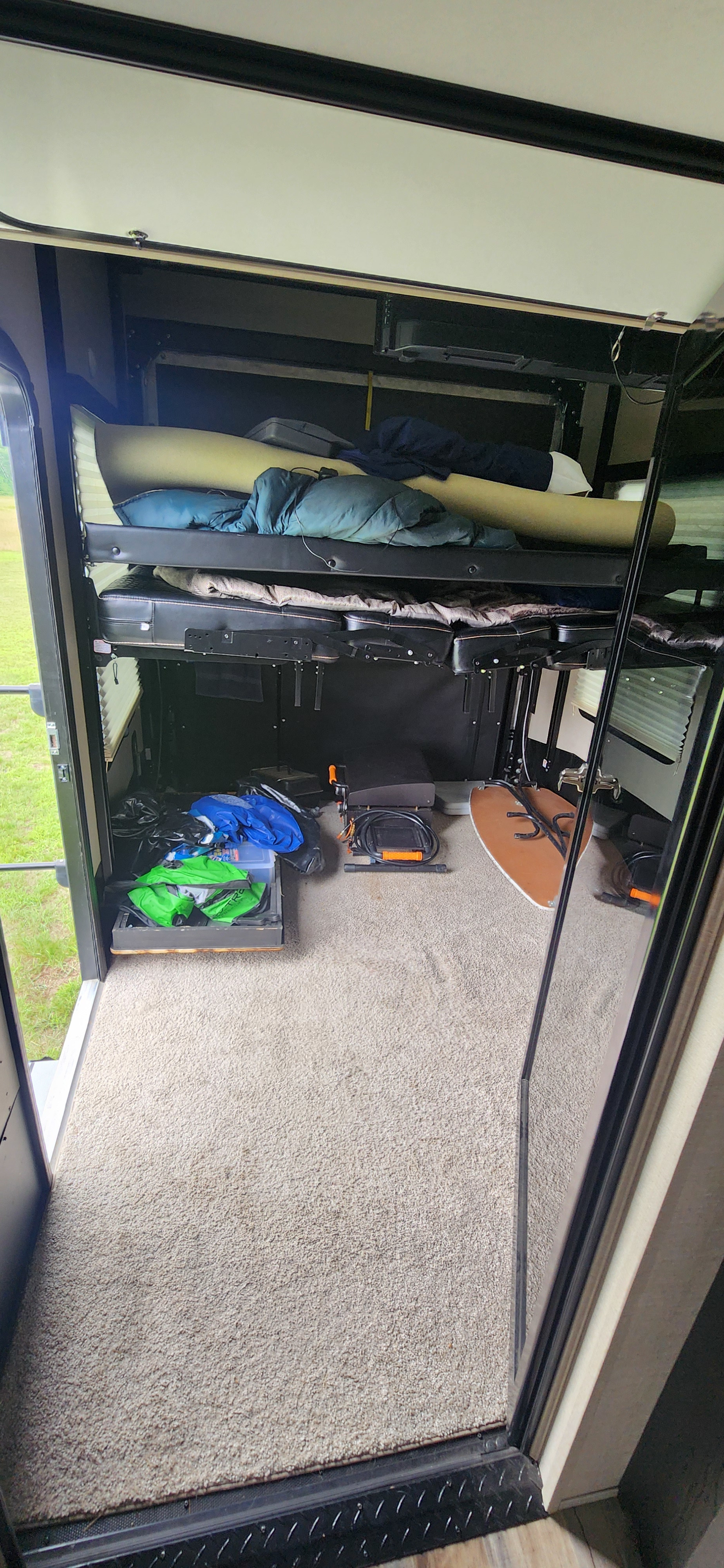 RV rental toy hauler interior, featuring convertible bunk beds and various gear stored on a carpeted floor, with the rear ramp door open.. Keystone Fuzion 2019