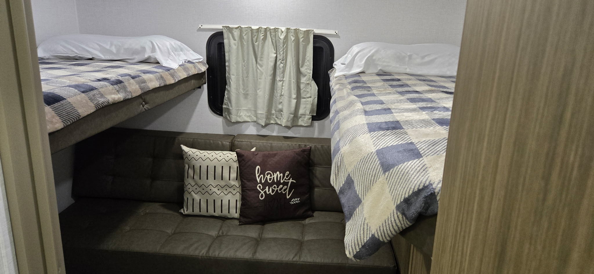 Cozy RV rental bunk room with two beds (one upper left, one right) and a sofa below a window with cushions.. Forest River Wildwood X-Lite 28VBXL 2026