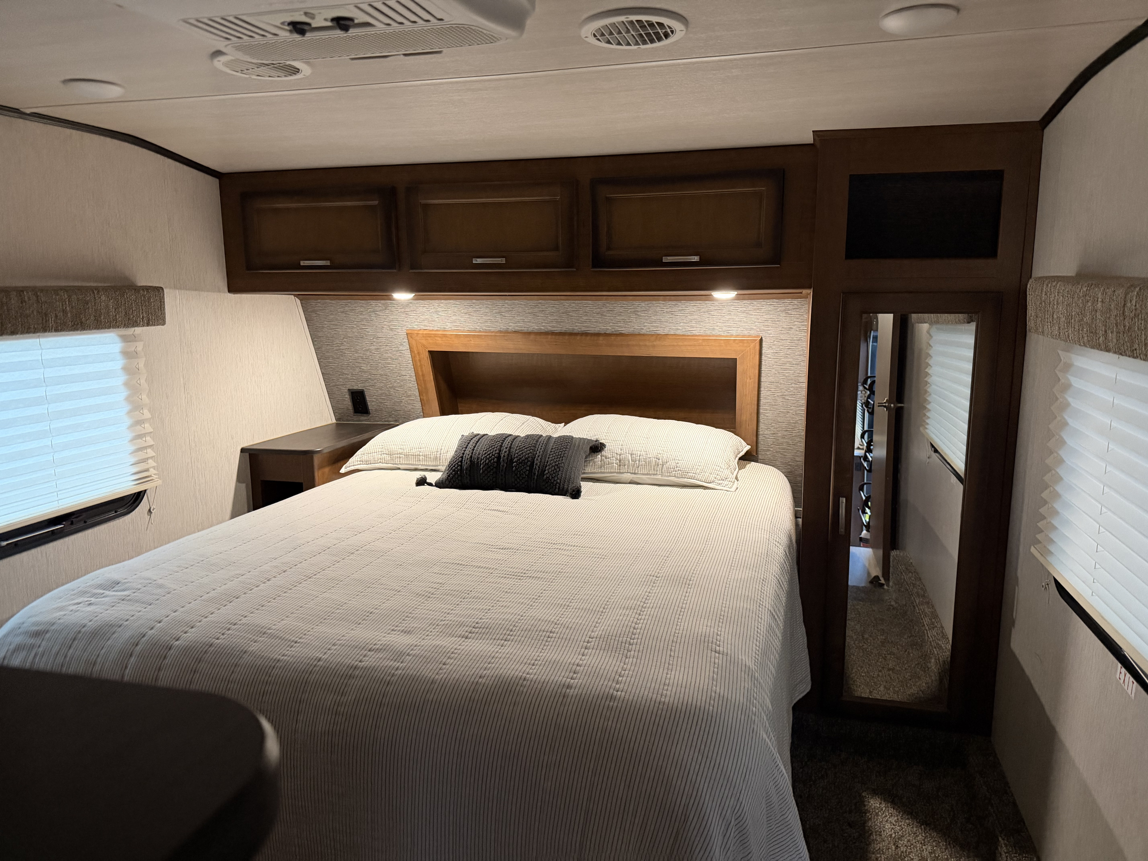 This inviting RV rental bedroom features a comfy bed with a striped comforter, overhead storage, and a full-length mirror.. Heartland RVs Prowler 2018