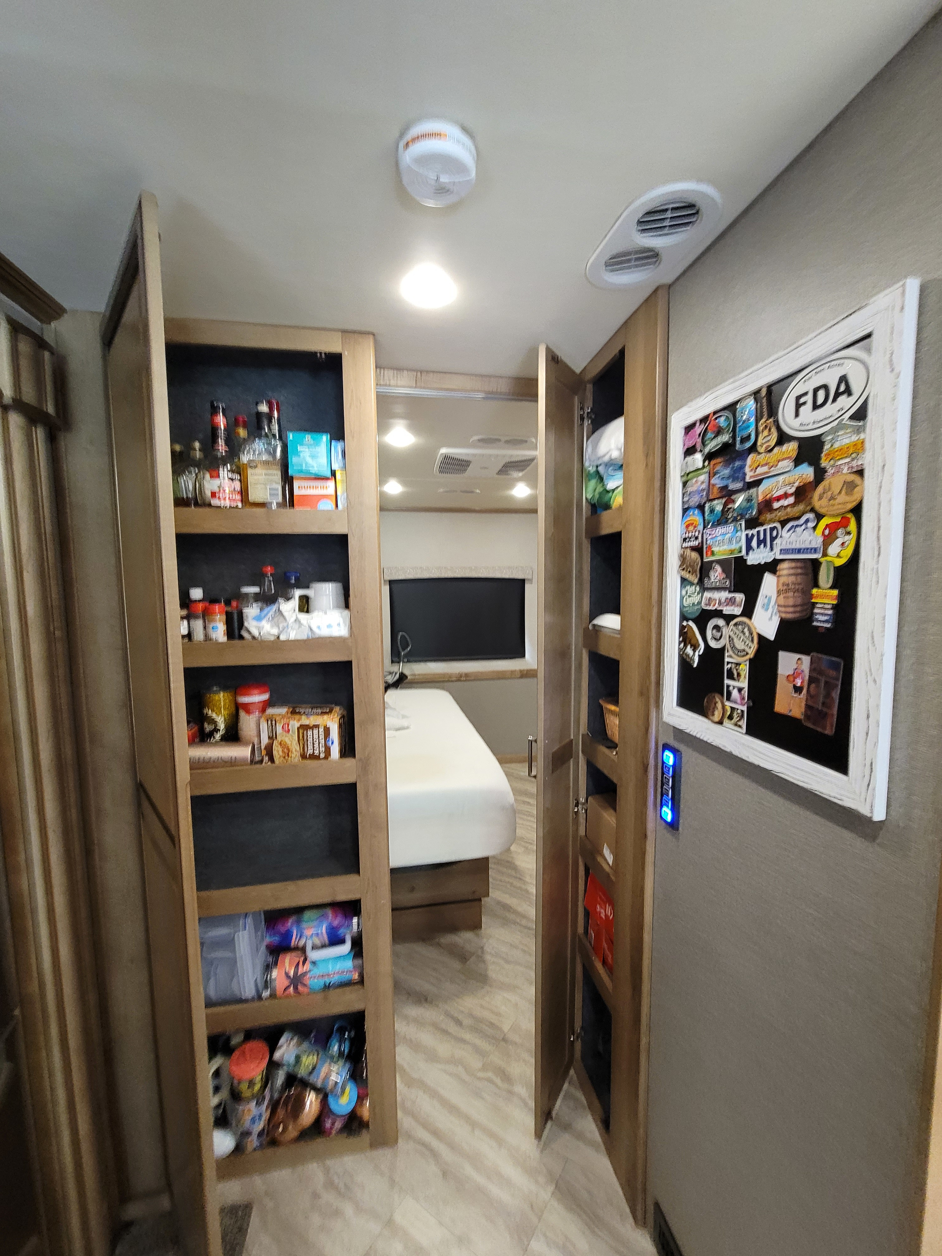 RV rental interior: two open pantries stocked with bottles & food items, a bedroom beyond, and a magnet board on the wall.. Fleetwood Southwind 36P 2019