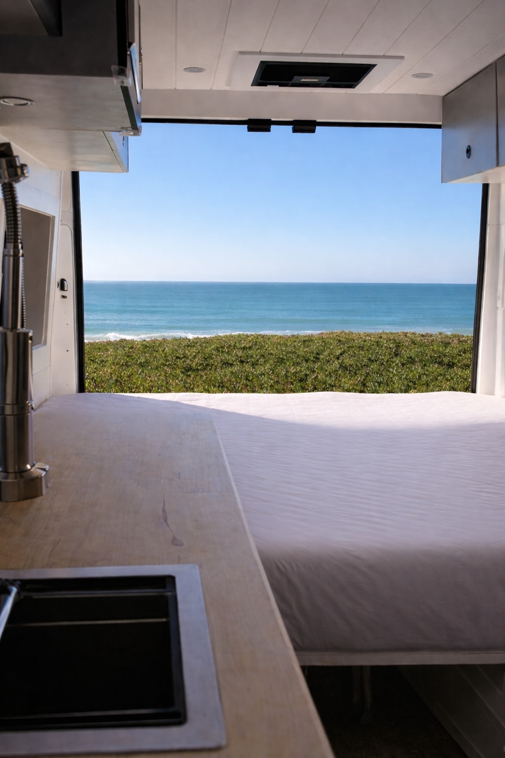 RV rental with ocean views! Inside a camper van, a bed on the right and a kitchen with a sink on the left face the sea.. Ram Promaster 2022