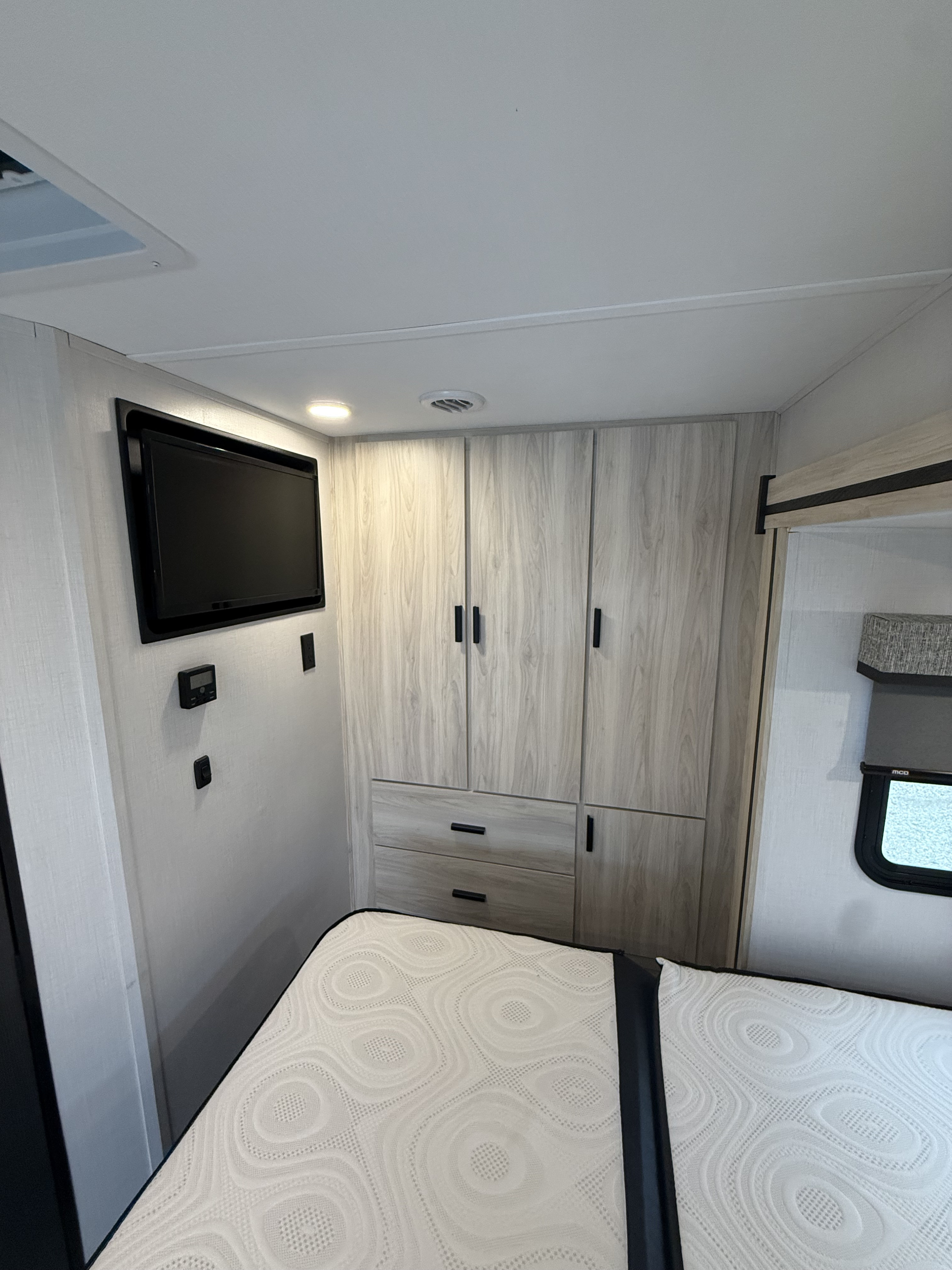 Cozy rv rental bedroom featuring a wall-mounted TV, light wood cabinets, and a patterned bed for a comfortable stay.. Forest River Sunseeker MBS 2022