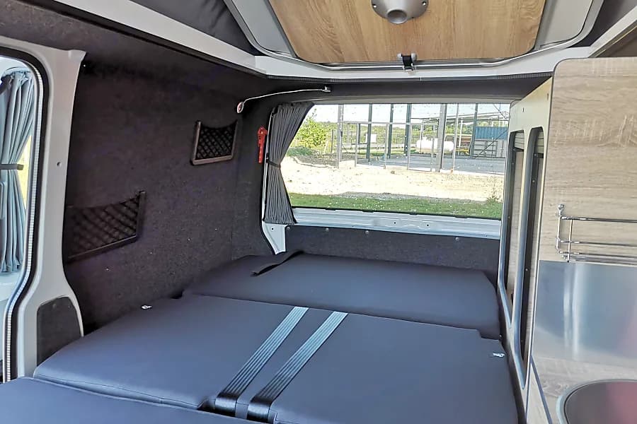 Cozy rv rental interior with a comfortable bed, storage nets, and built-in kitchenette, perfect for travel.. Volkswagen T6.1 Globe Trotter 2025