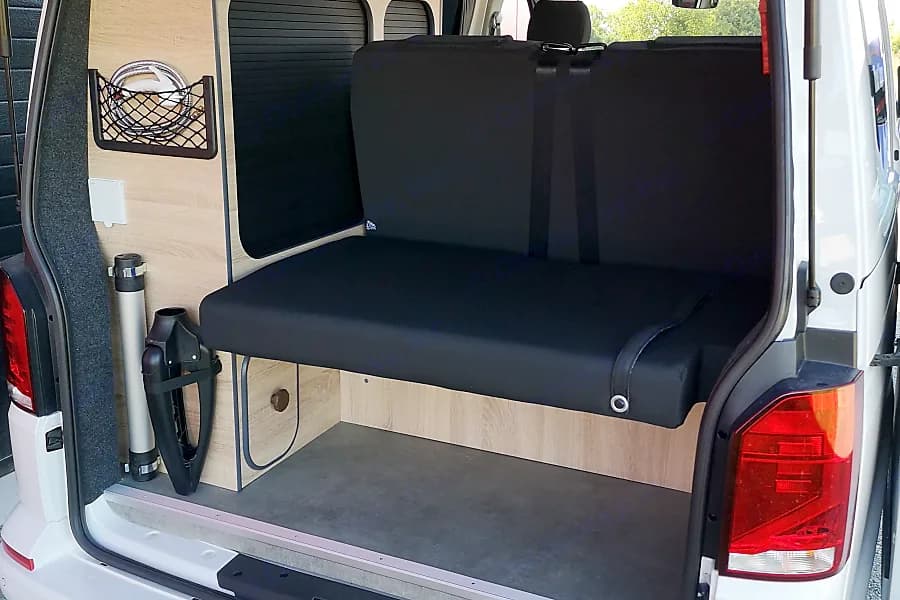 RV rental campervan's interior: rear black bench seat converts to a bed, with wood paneling and mesh storage.. Volkswagen T6.1 Globe Trotter 2025