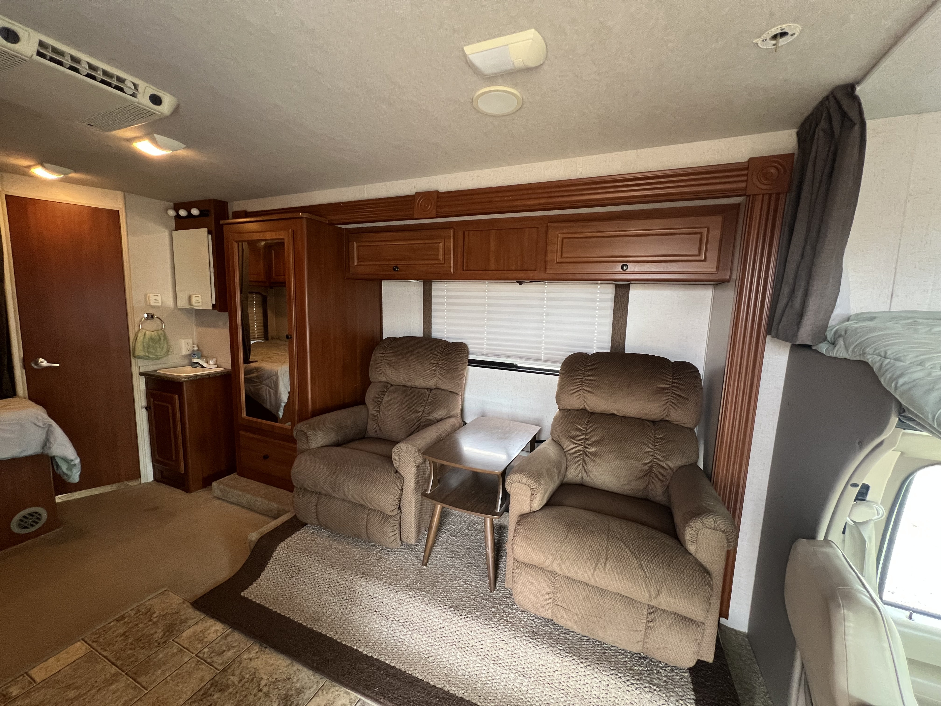 Cozy RV rental interior with recliners, wooden cabinets, and a window, ideal for comfortable travel.. Tioga Ranger 2009
