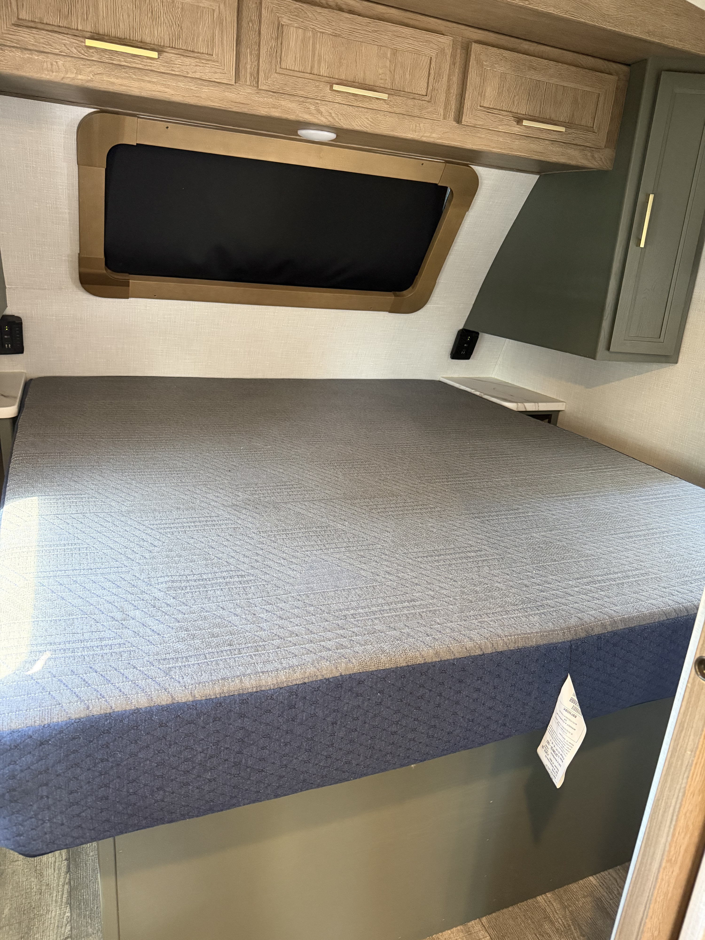 RV rental bedroom: cozy bed with grey mattress, overhead cabinets, window, and convenient charging ports.. Dutchmen Eddie Bauer 2023