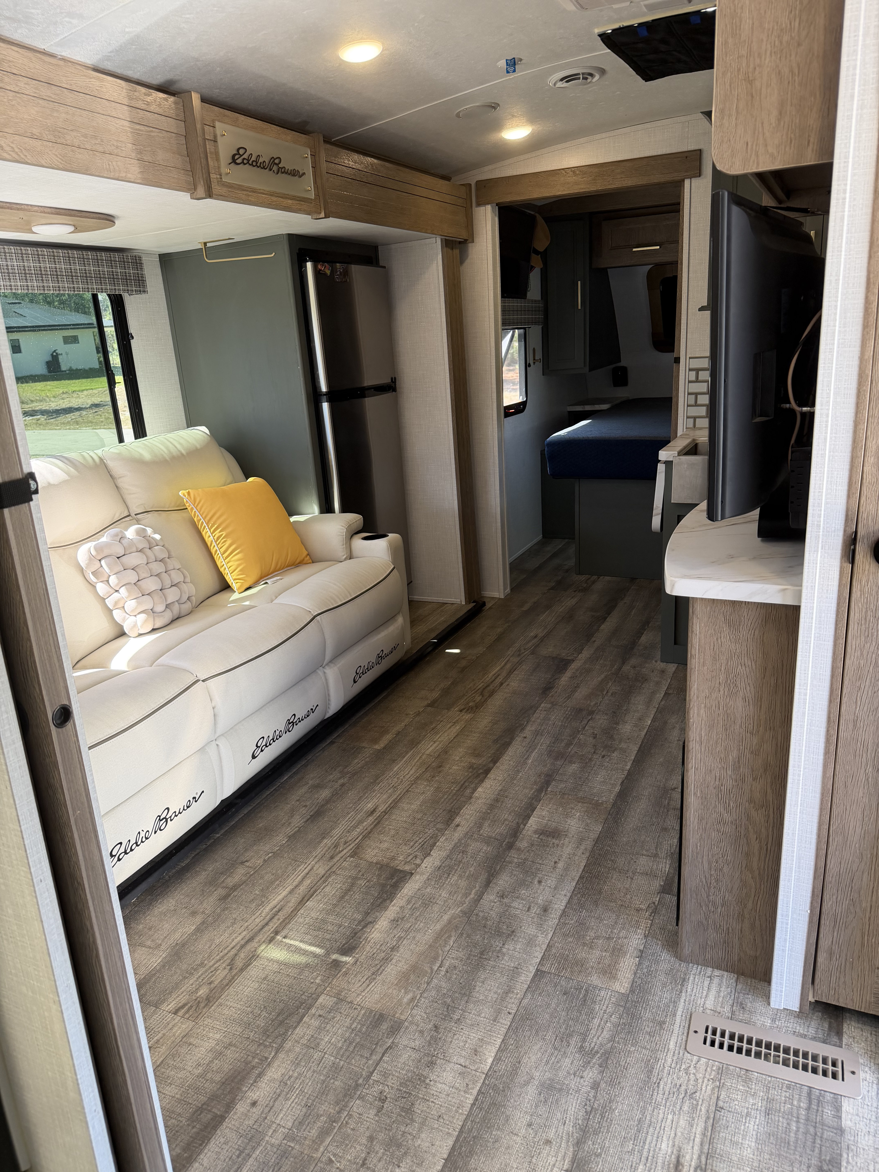 Explore this bright Eddie Bauer rv rental interior with a comfy sofa, modern features, and a glimpse of the bedroom.. Dutchmen Eddie Bauer 2023