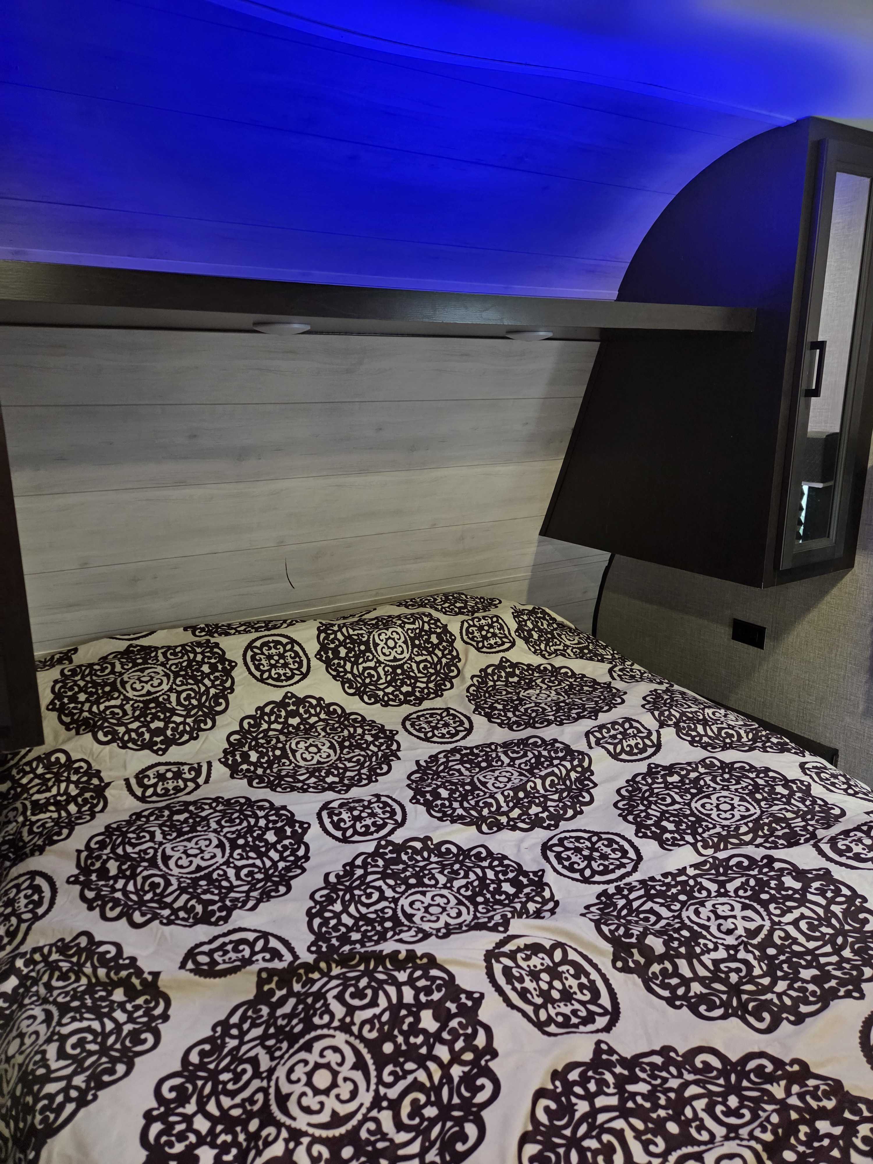 Cozy RV rental bedroom featuring a bed with patterned duvet, blue LED lighting, and overhead storage.. Jayco Jay Flight SLX Rocky Mountain Edition 2022