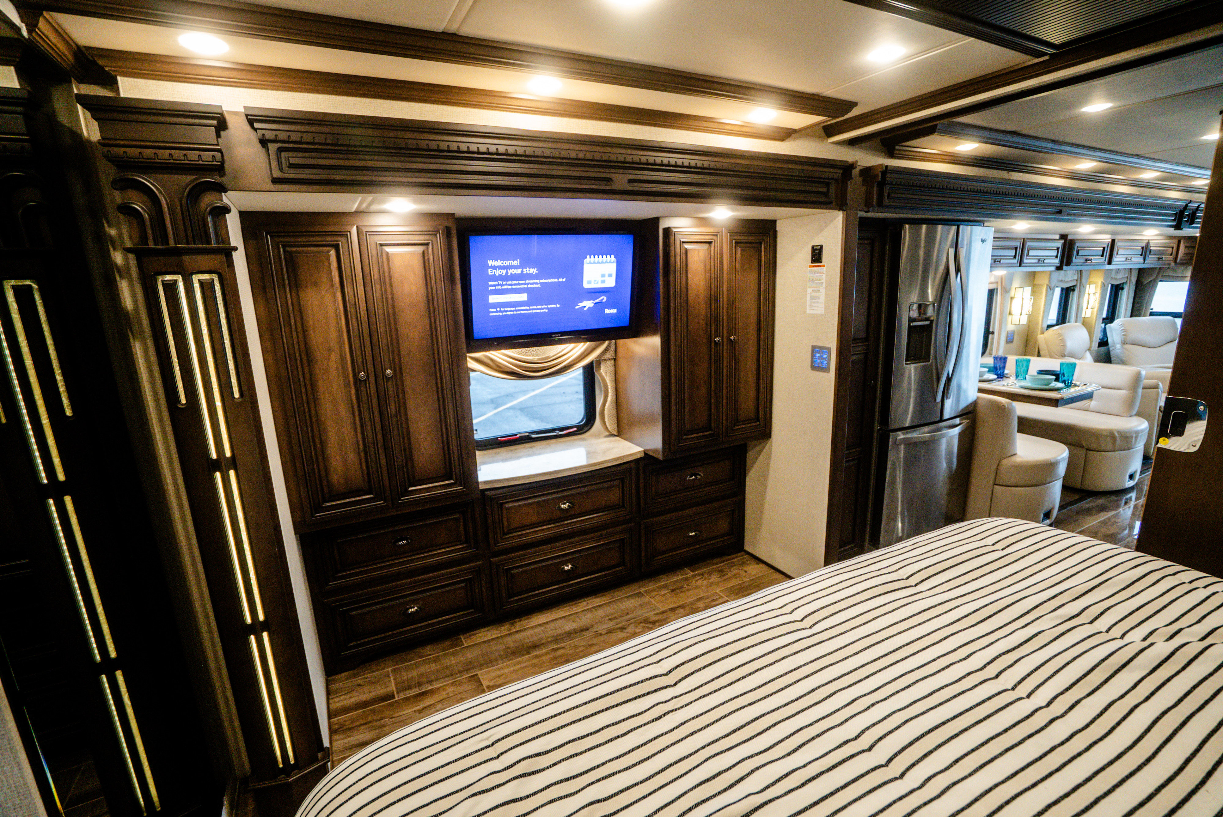 Luxury RV rental bedroom and living area, featuring a striped bed, dark wood cabinetry, and a stainless steel fridge.. Dutch Star Dutch Star Motorhome 2018