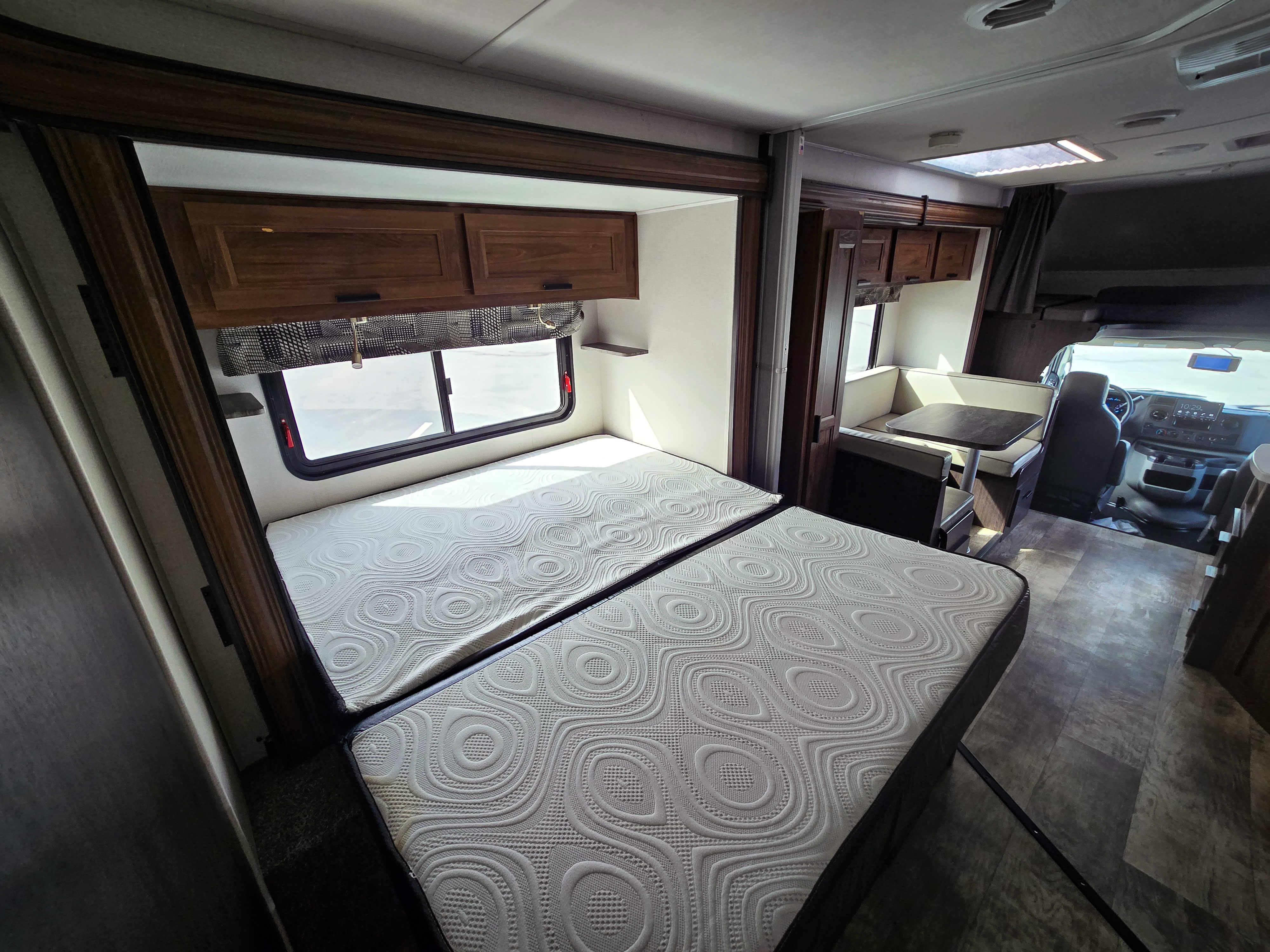 Modern rv rental interior showing a sleeping area with two beds, a dinette, and the driver's cockpit. Ready for adventure!. Forest River Sunseeker Classic 2023