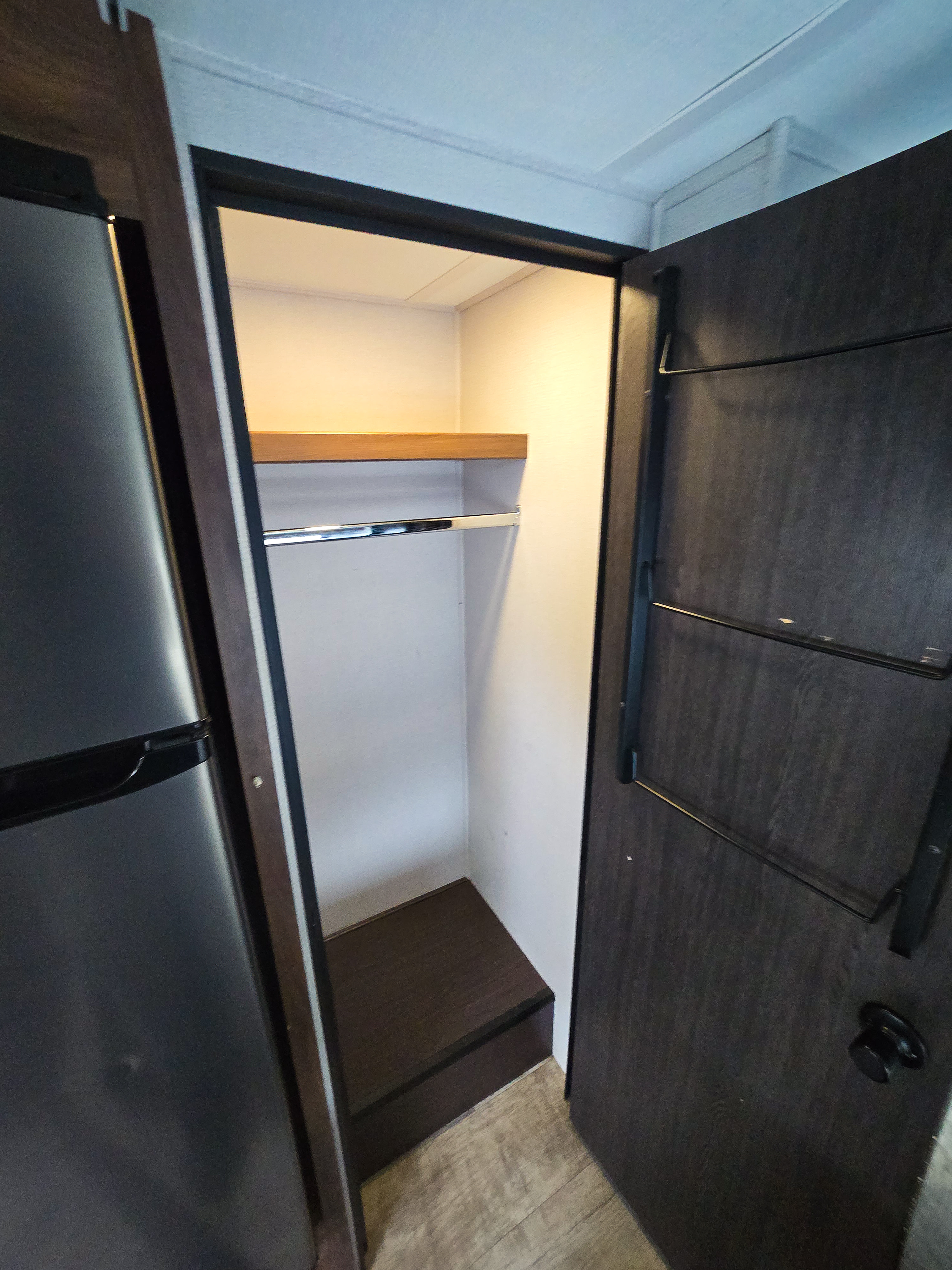 RV rental interior showing an open closet with a shelf, hanging rod, door storage, and adjacent refrigerator.. Forest River Sunseeker Classic 2023