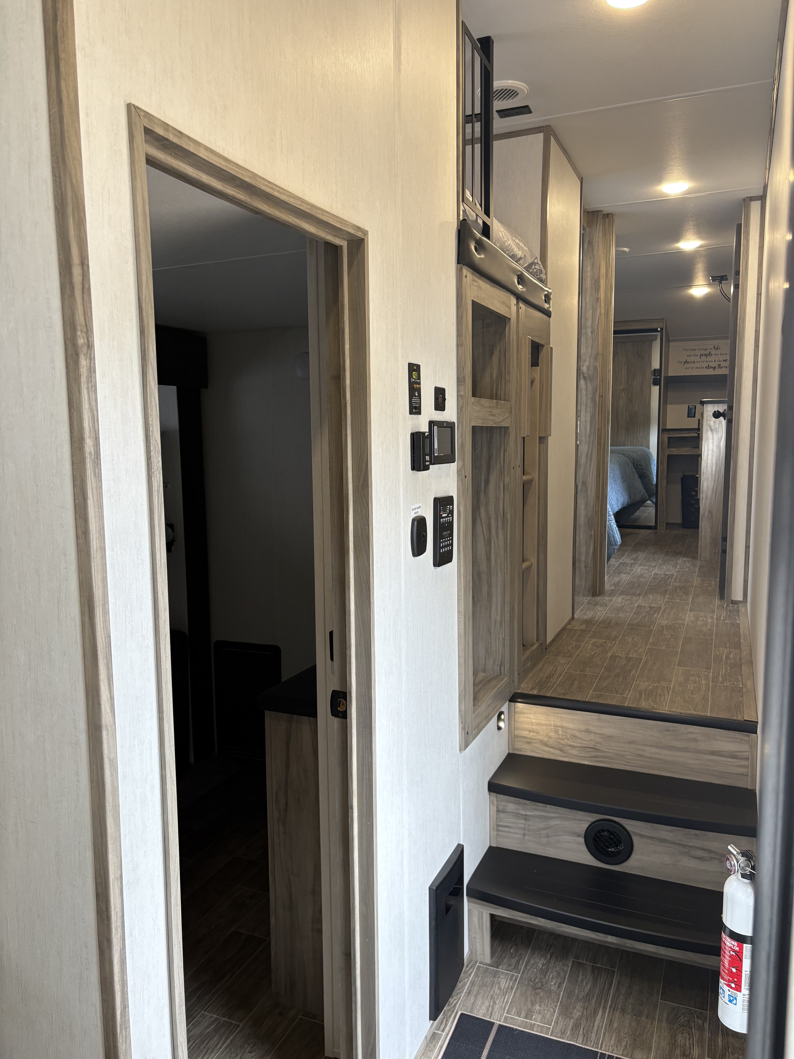 Modern RV rental interior: bright hallway, control panel, & stairs lead to a cozy bunk area and rear bedroom.. Forest River Cherokee Arctic Wolf 2022