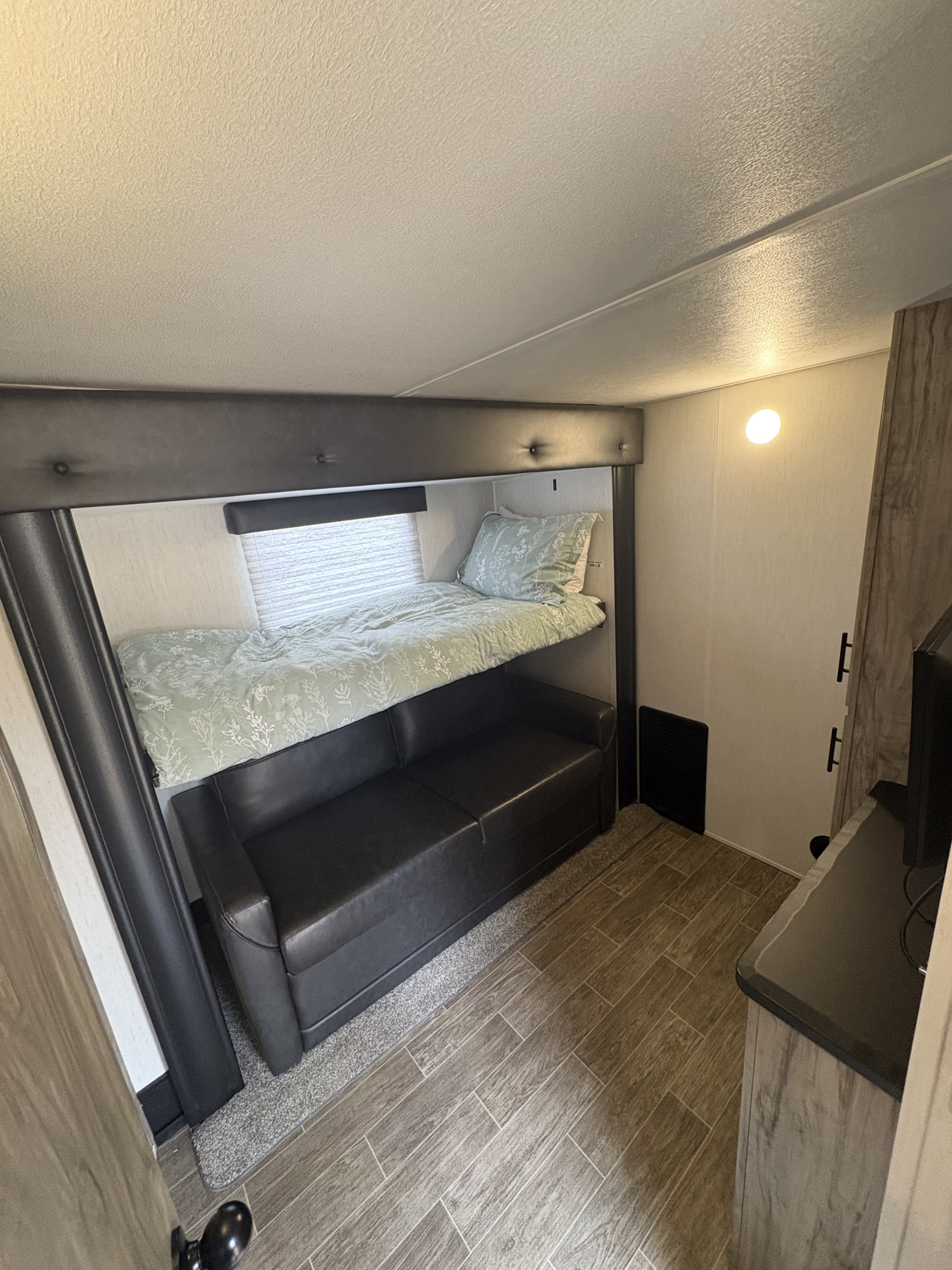 Step into this inviting rv rental, featuring a bunk bed with a floral comforter above a dark sofa, wood-look flooring, and ceiling light.. Forest River Cherokee Arctic Wolf 2022