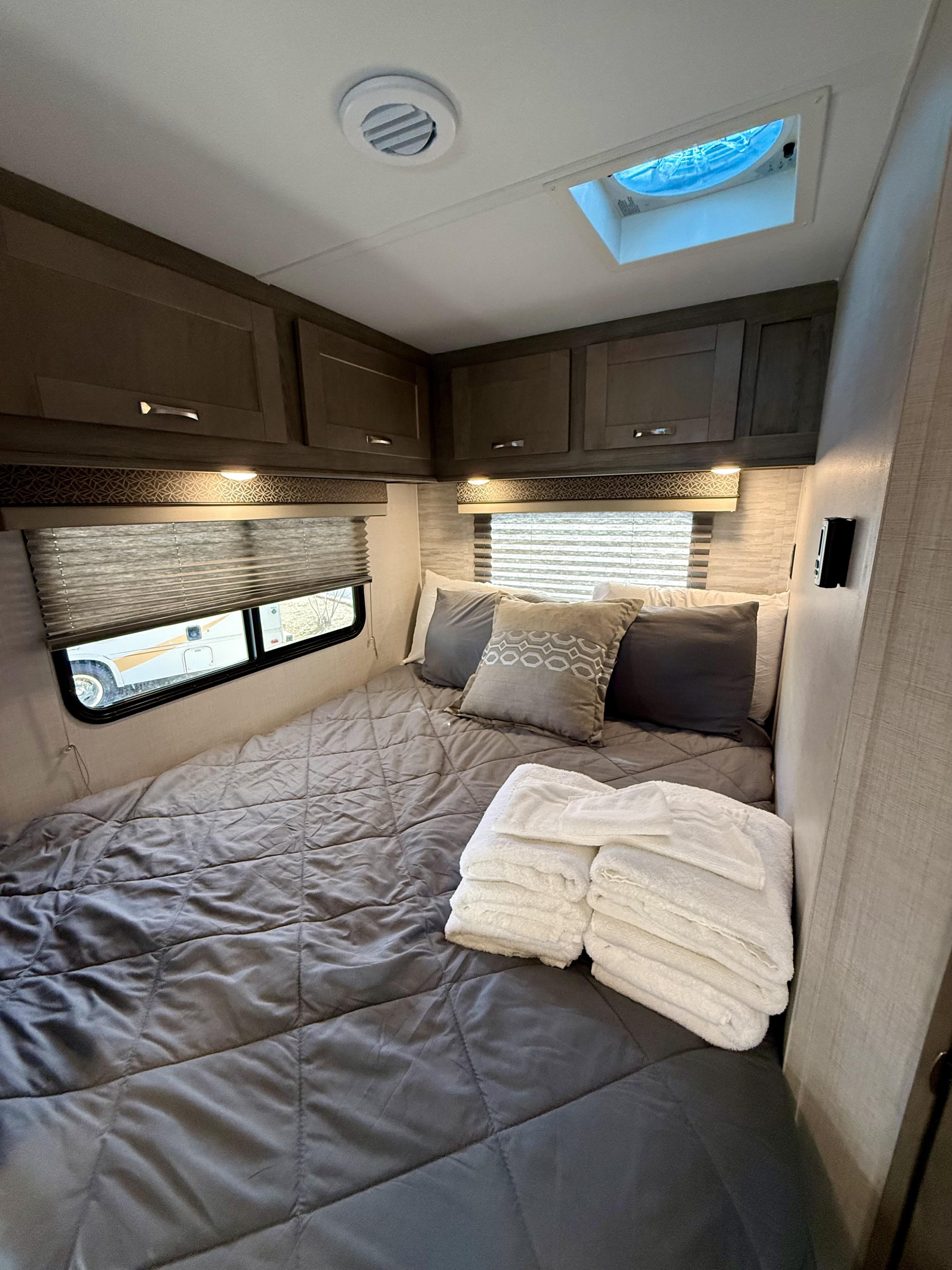Cozy RV rental bedroom with grey bedding, pillows, fresh white towels, overhead cabinets, and a skylight.. Gulf Stream Conquest 2024