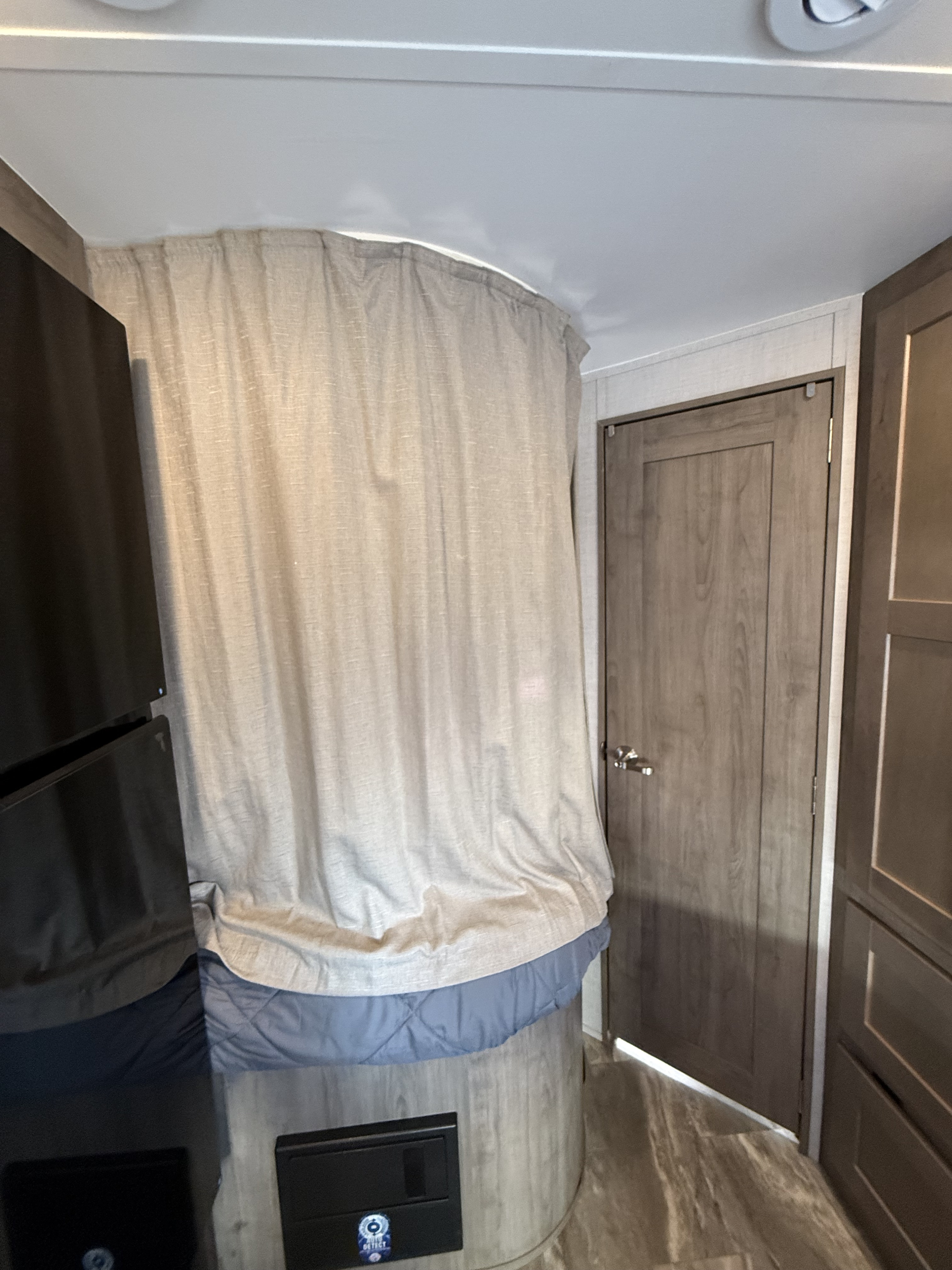 Interior of an rv rental showing a privacy curtain for a sleeping area, a refrigerator, a door, and storage cabinets.. Gulf Stream Conquest 2024