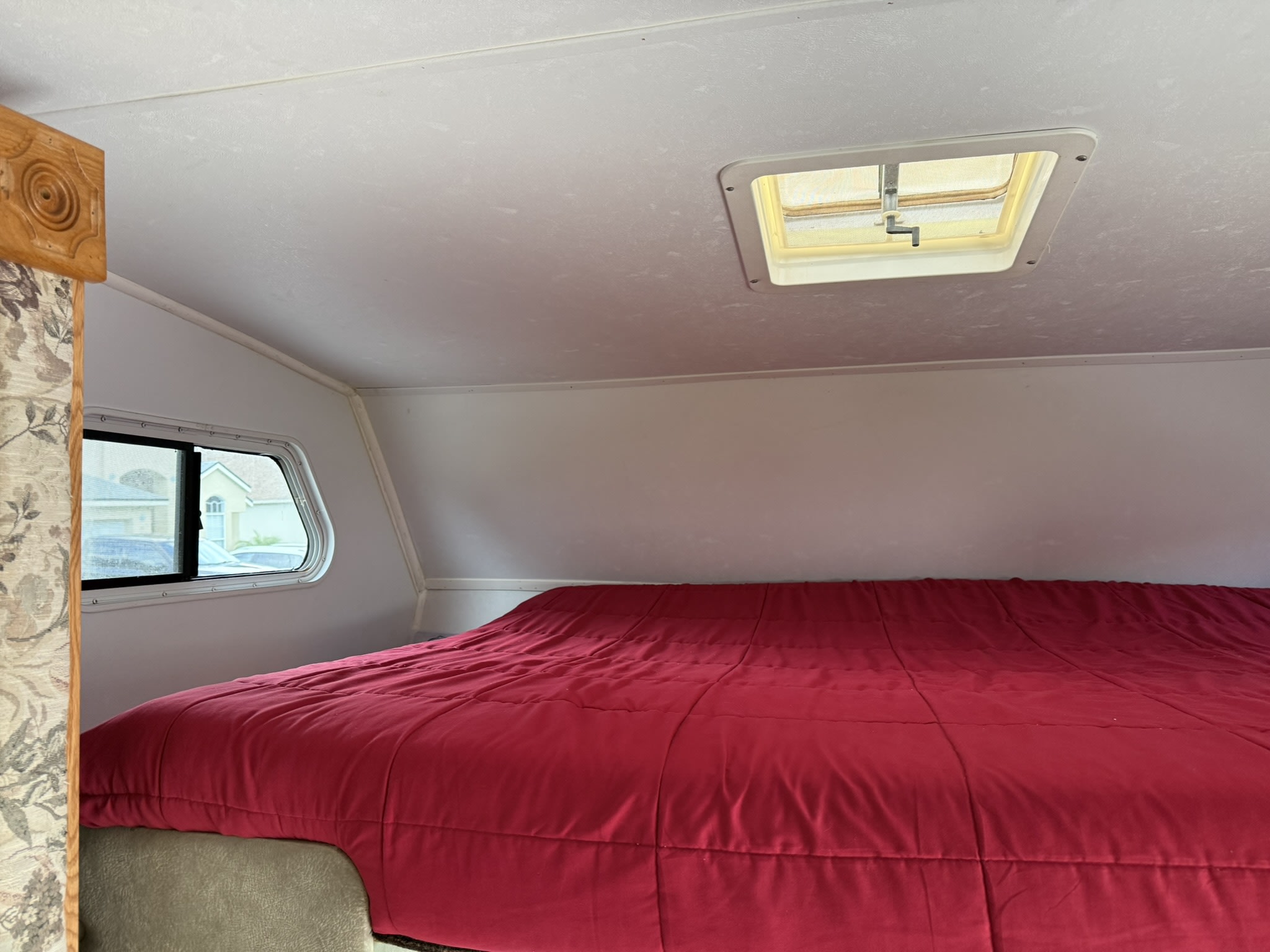 Cozy RV rental bedroom featuring a plush red comforter, overhead skylight, and side window, ready for rest.. Ford e450 condor 2003