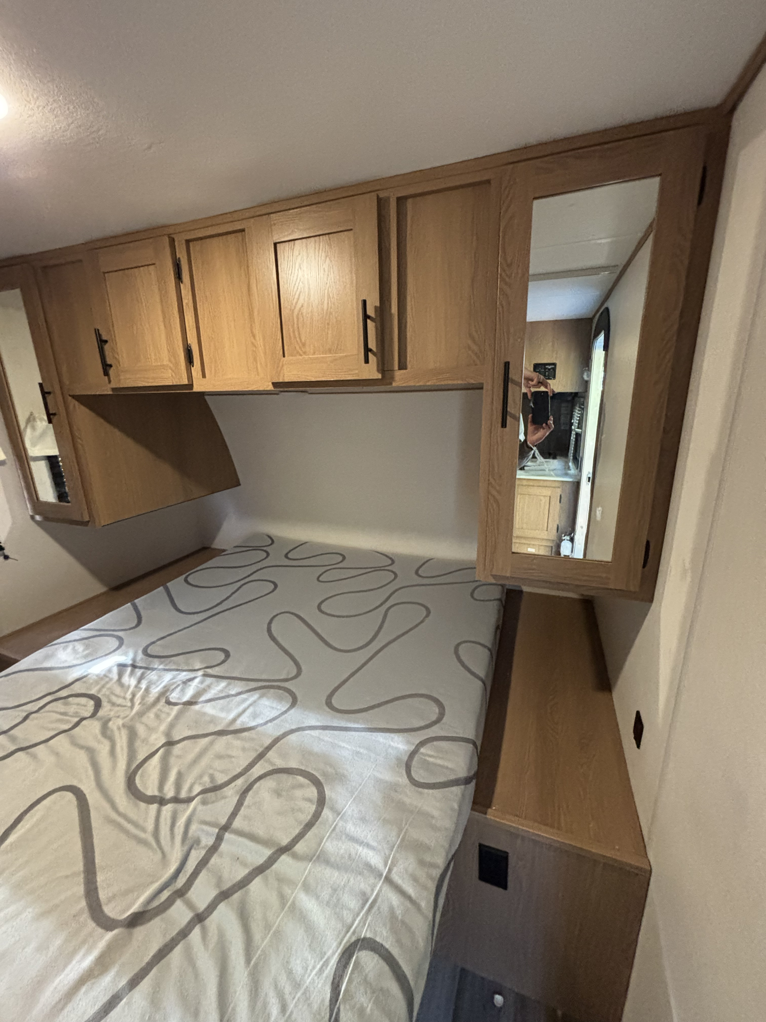 Cozy RV rental bedroom featuring overhead wooden cabinets, bedside mirrors, and a bed with a modern patterned sheet.. Avenger Avenger Trailer 2022