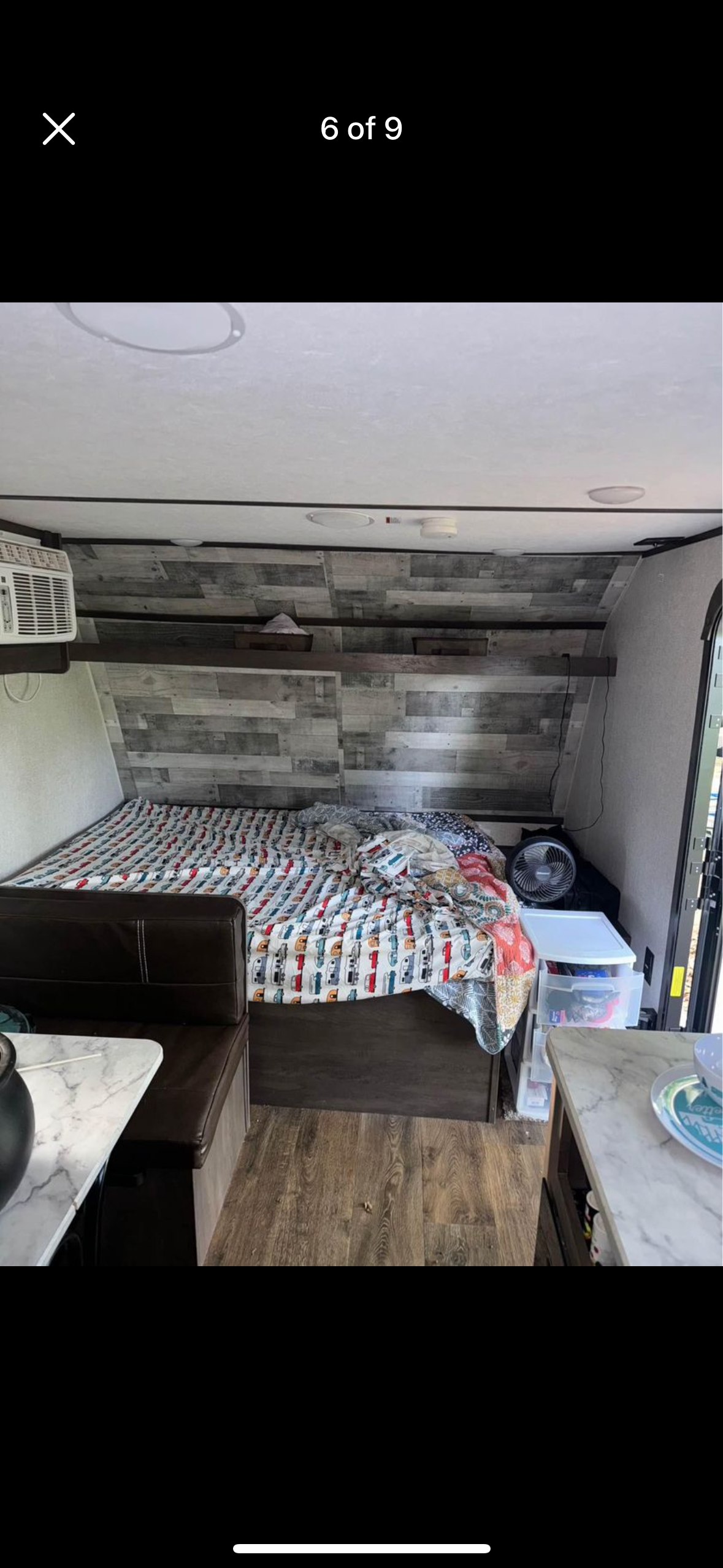 RV rental interior: bed with colorful quilt, dinette, AC unit, and storage solutions in a wood-paneled compact space.. Dutchmen Coleman Lantern LT 2021