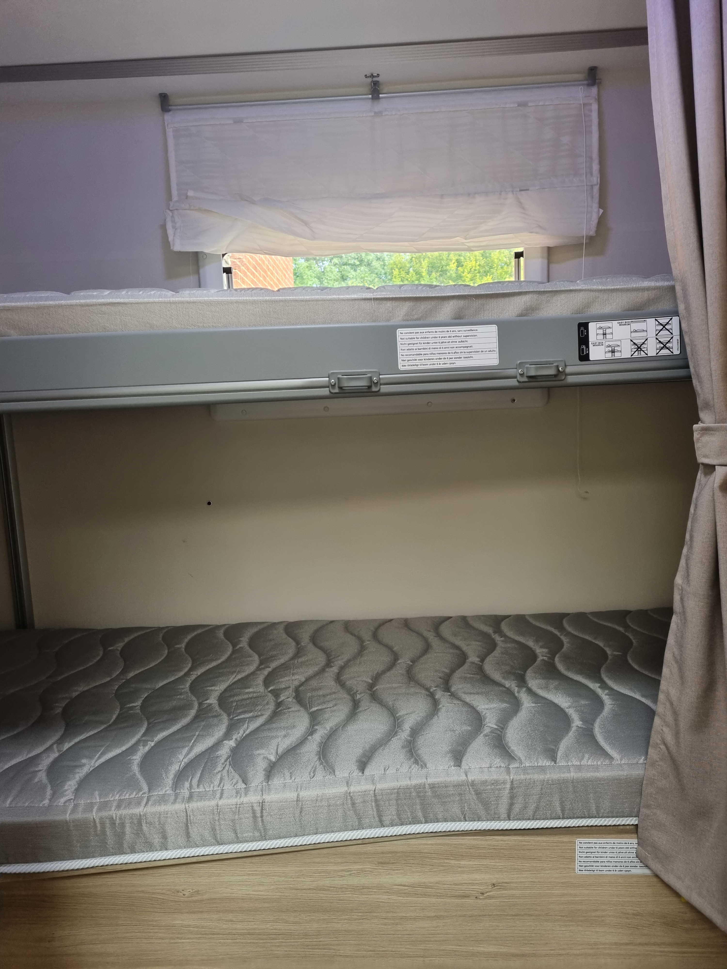 Cozy bunk beds in an RV rental, featuring mattresses, a window with a blind, and important safety warnings for users.. Chausson 720 VIP Titanium 2021
