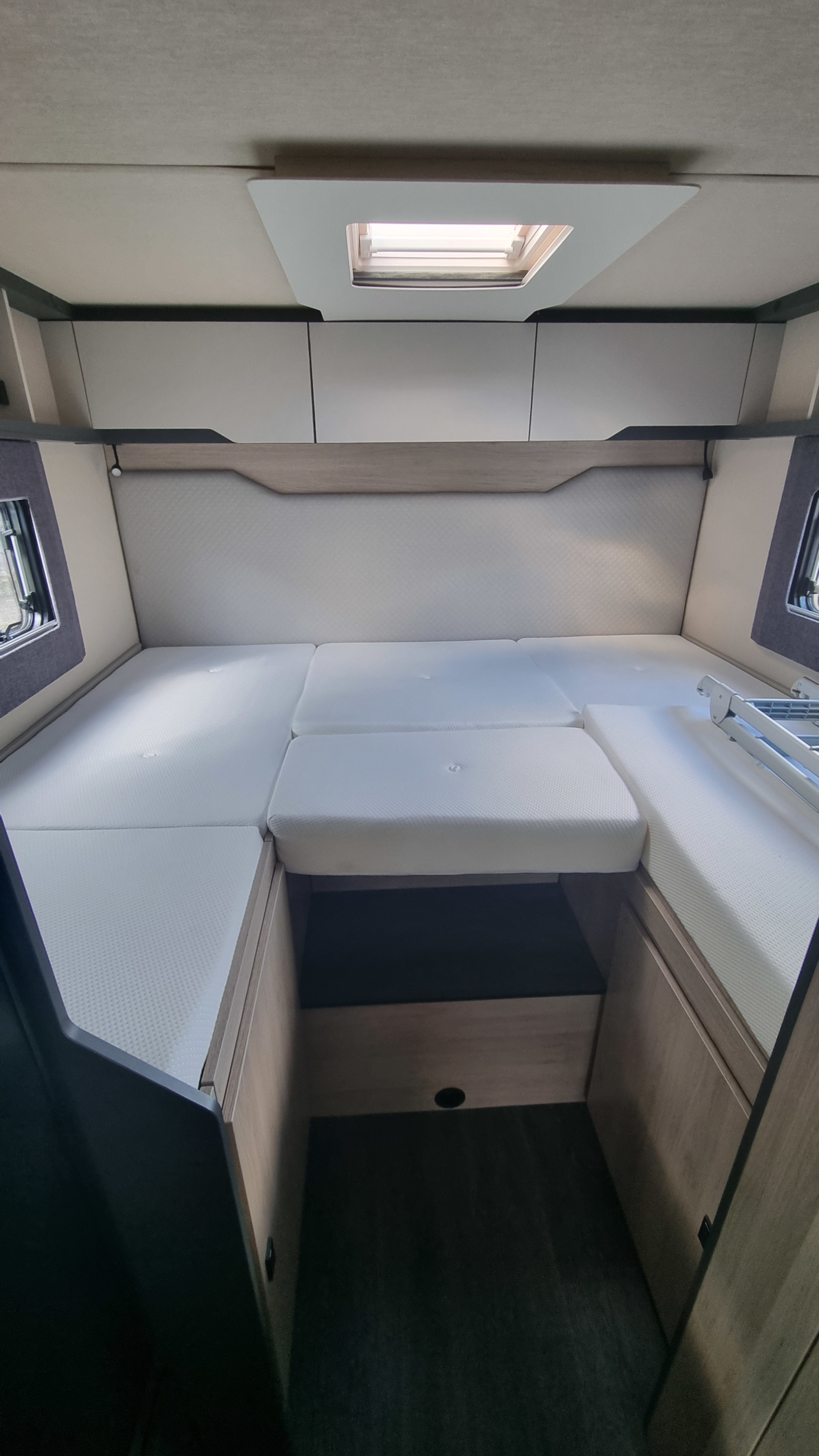 Inside a modern RV rental: a flexible sleeping area featuring white mattresses, overhead storage, side windows, and a skylight.. Auto-Trail F70 2025